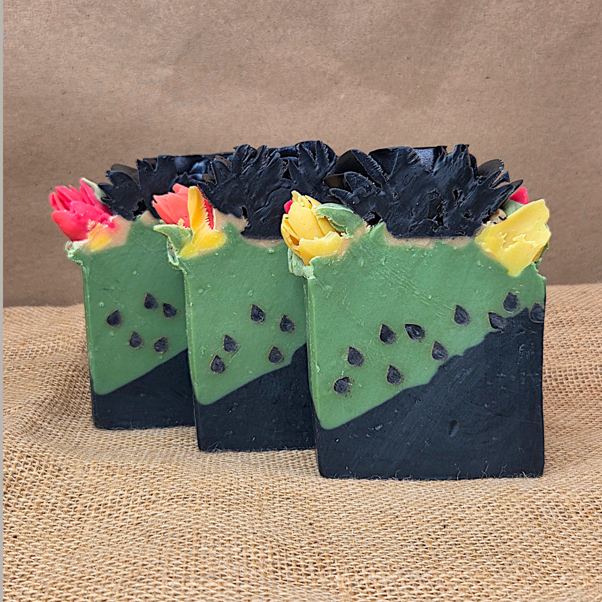 Three cactus-shaped soap bars with floral decorations on a textured surface.