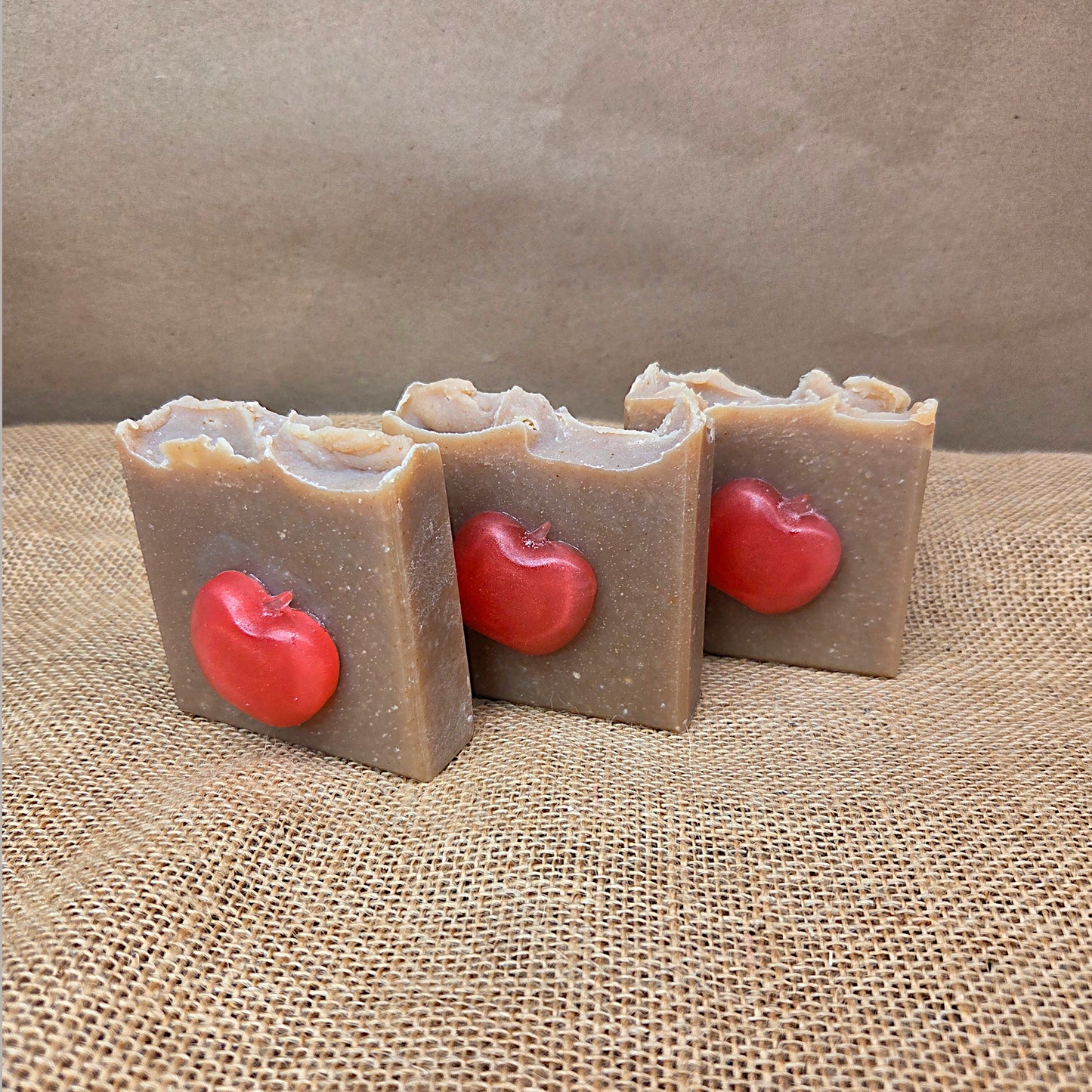Three bars of soap with red apple decorations on a textured brown surface