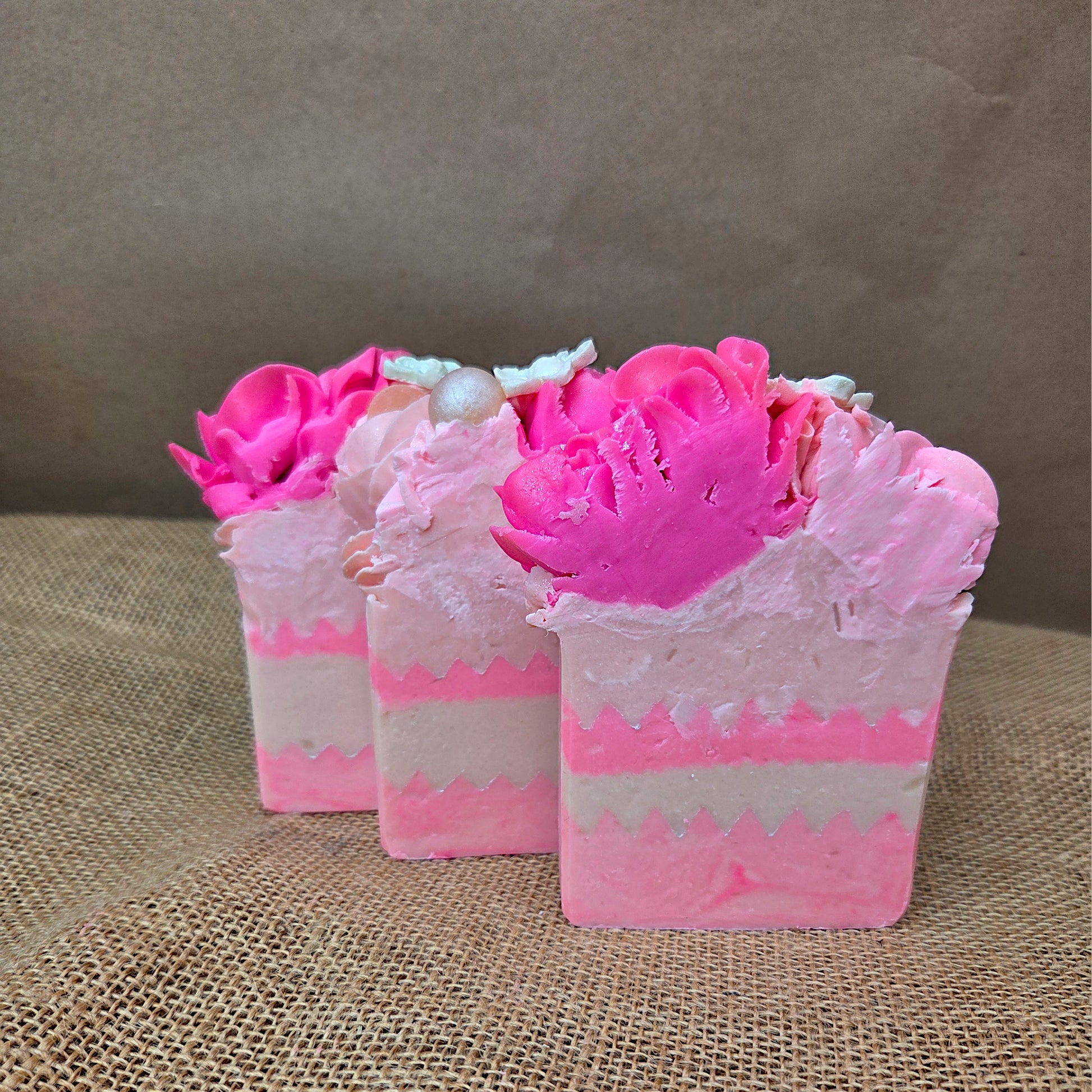 Three pink and white soap bars with floral designs on a textured surface.