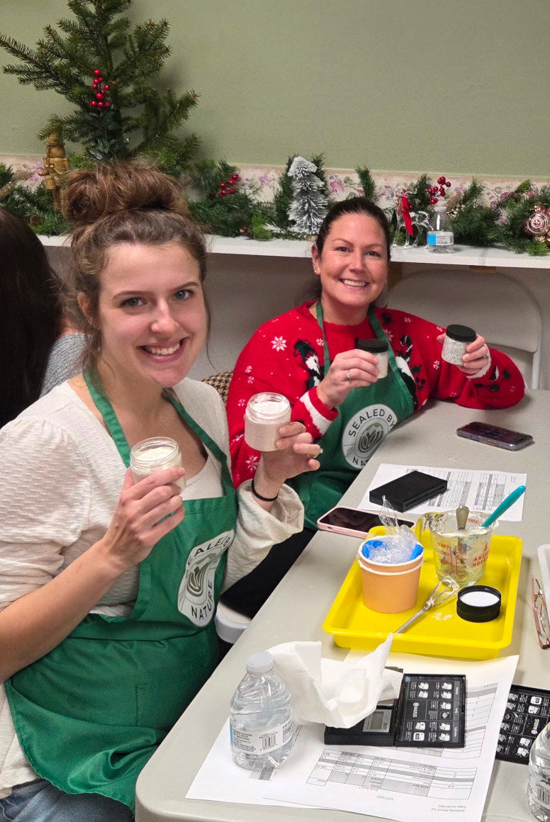 Two women in green aprons sitting at a table with Christmas decorations in the background.