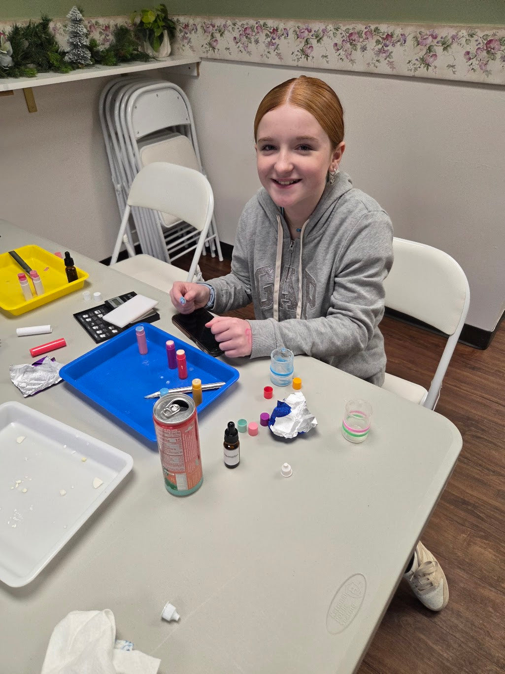 Person sitting at a table with science experiment materials, making lip balm.