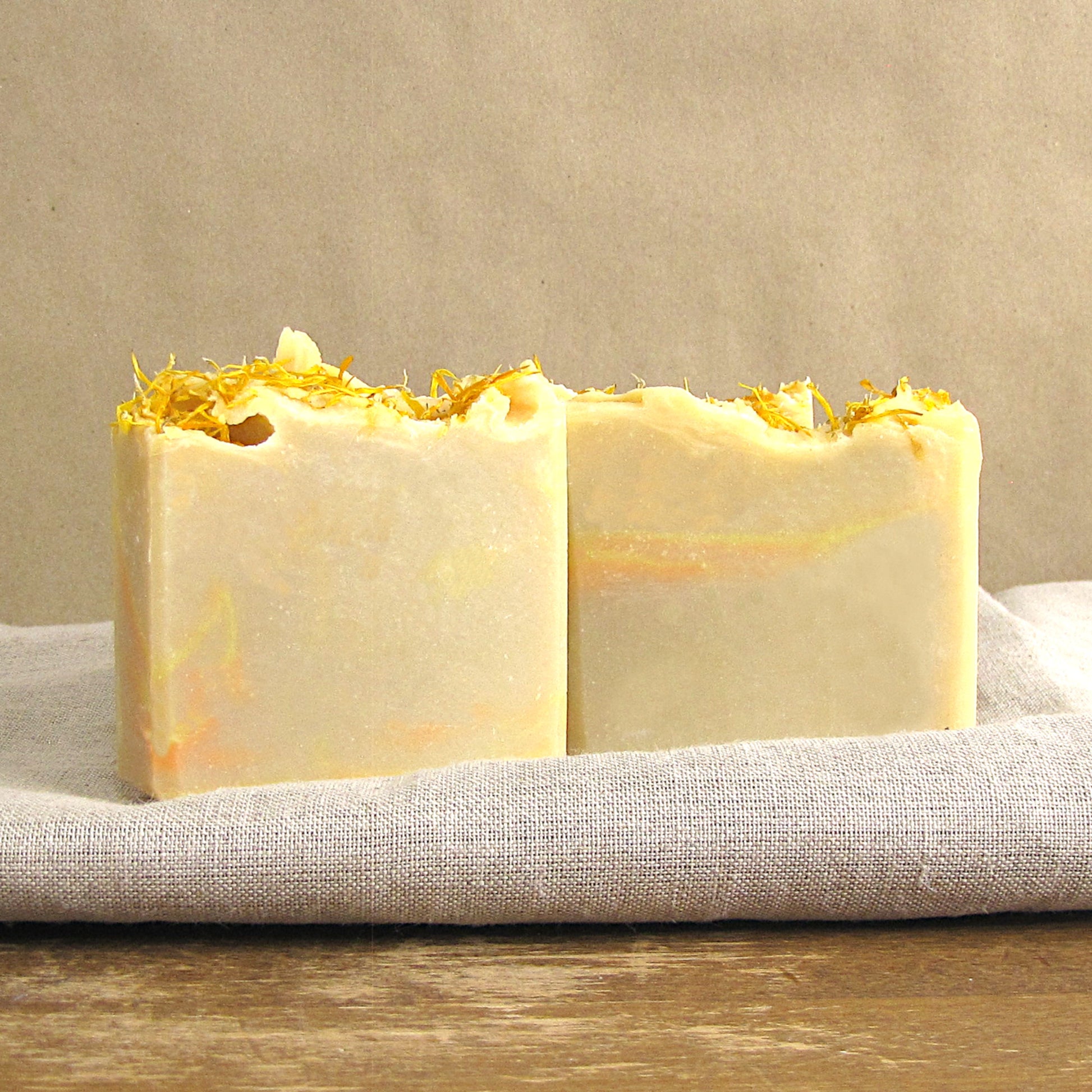 Two bars of soap with yellow flower petals on a beige background