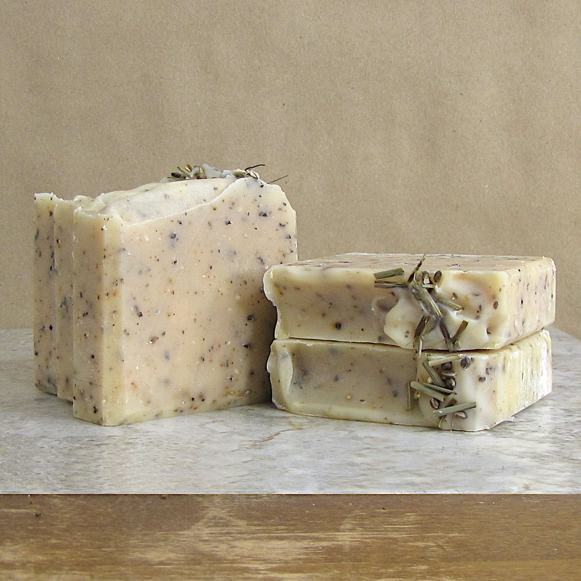 Multiple bars of soap with hemp seeds and dried lemongrass leaves on a marble surface.