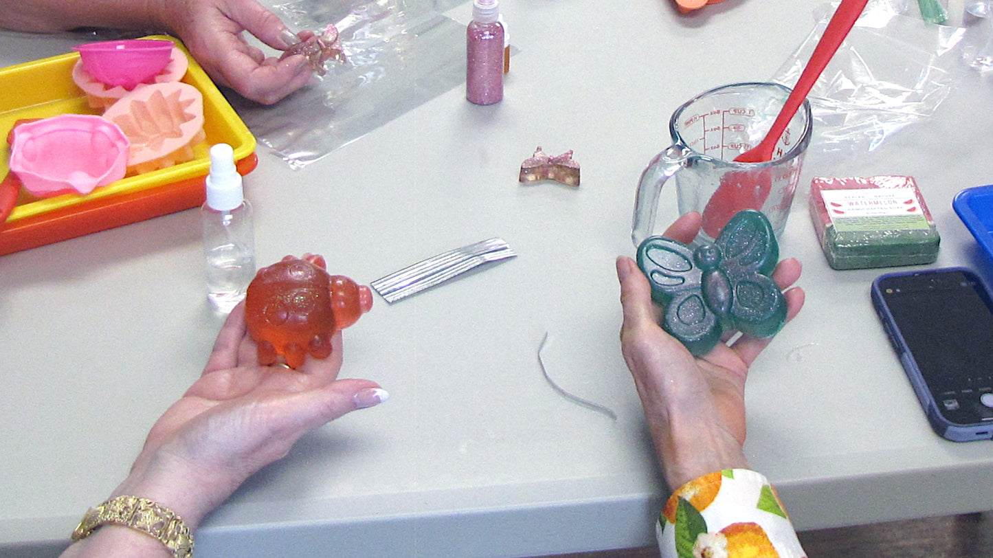 Hands holding colorful butterfly and ladybug soaps made with melt and pour soap.