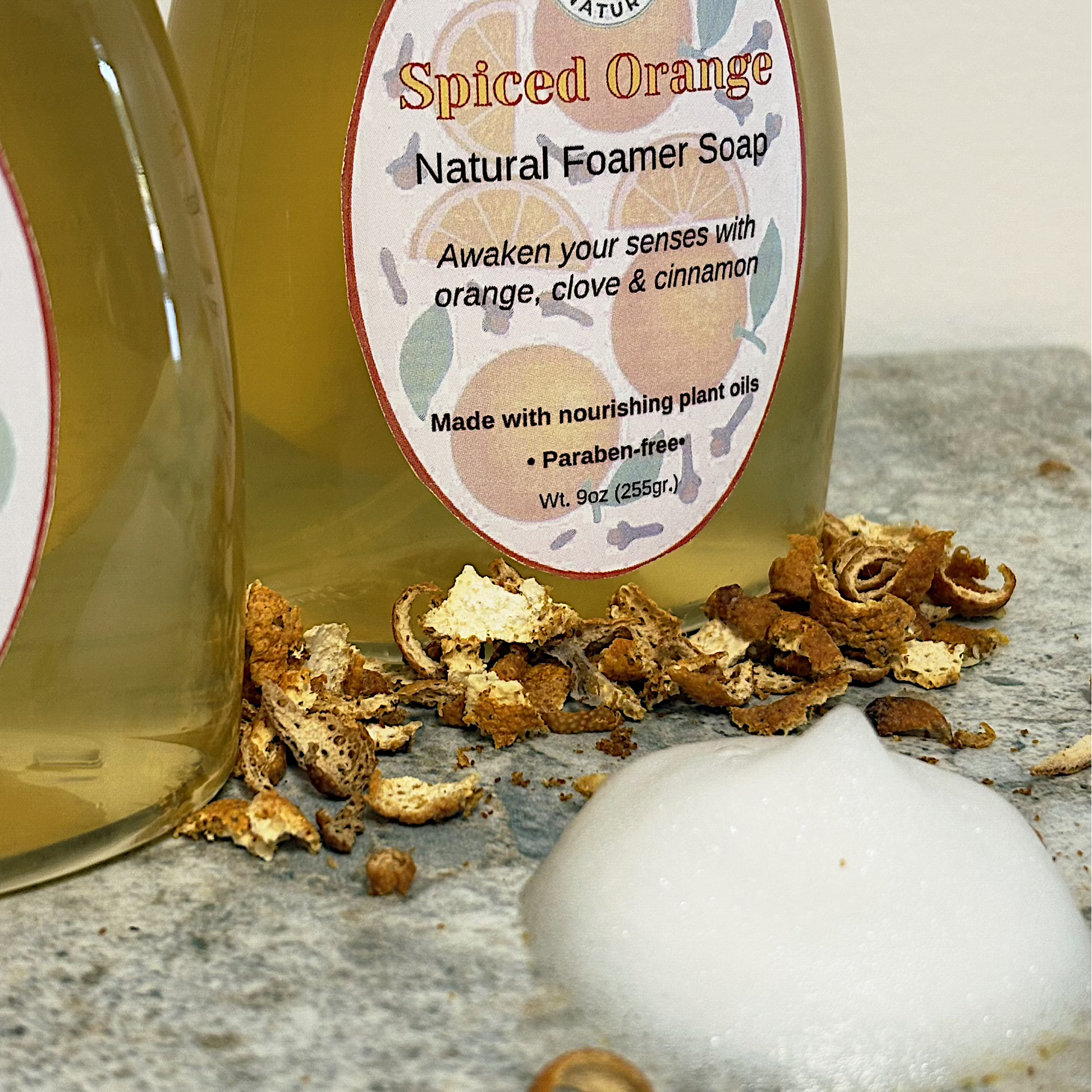 Spiced Orange natural foamer soap with a label, cinnamon sticks, and a bath bomb on a stone surface.
