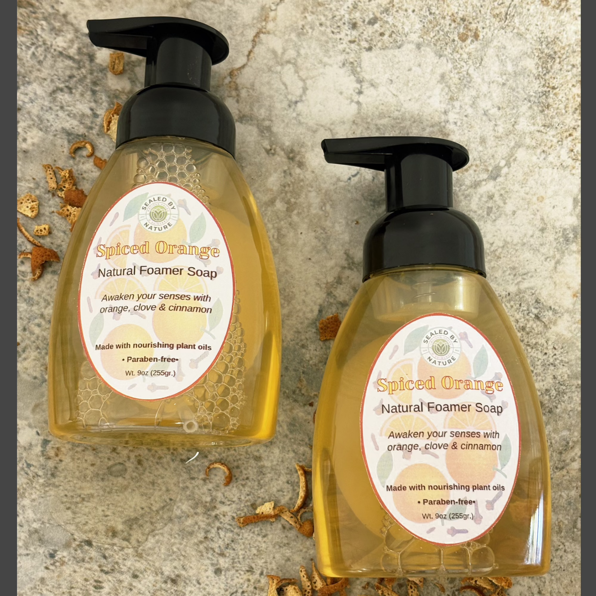 Two bottles of Spiced Orange Natural Foamer Soap on a stone surface with dried orange peels.