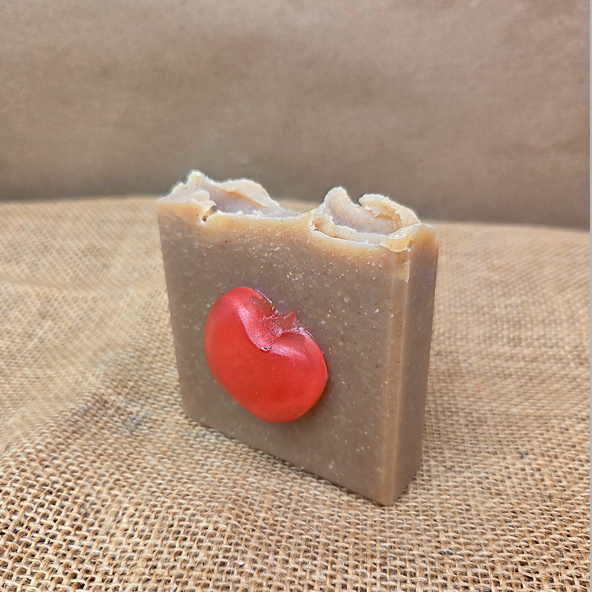 Bar of soap with a red cherry on top on a burlap surface