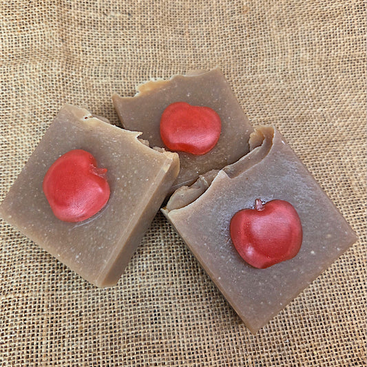 Three square brown candies with red apple-shaped centers on a textured beige background