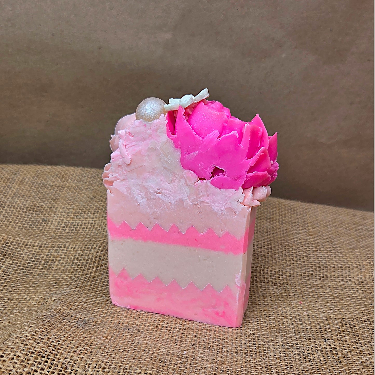 Pink and white soap bar with a decorative flower on a brown textured surface