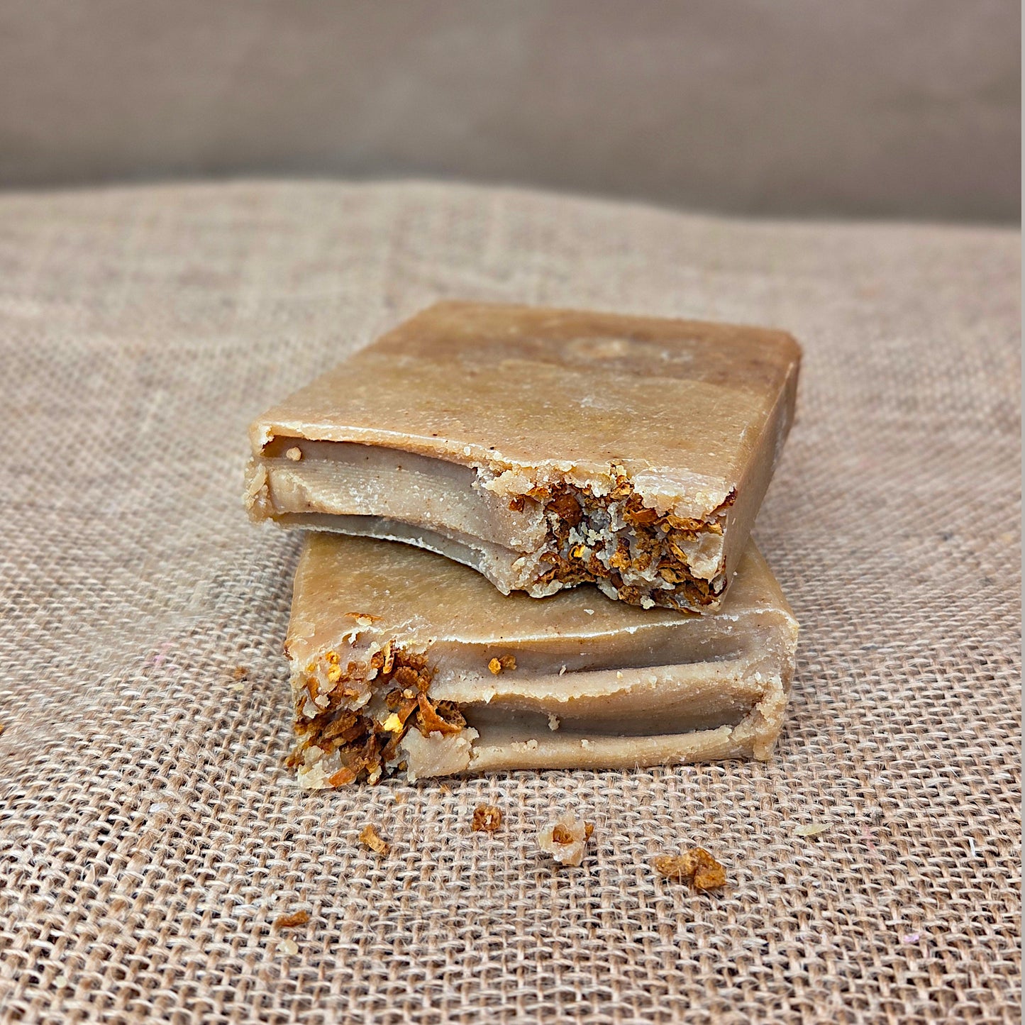 Two pieces of soap with visible ingredients on a textured fabric background
