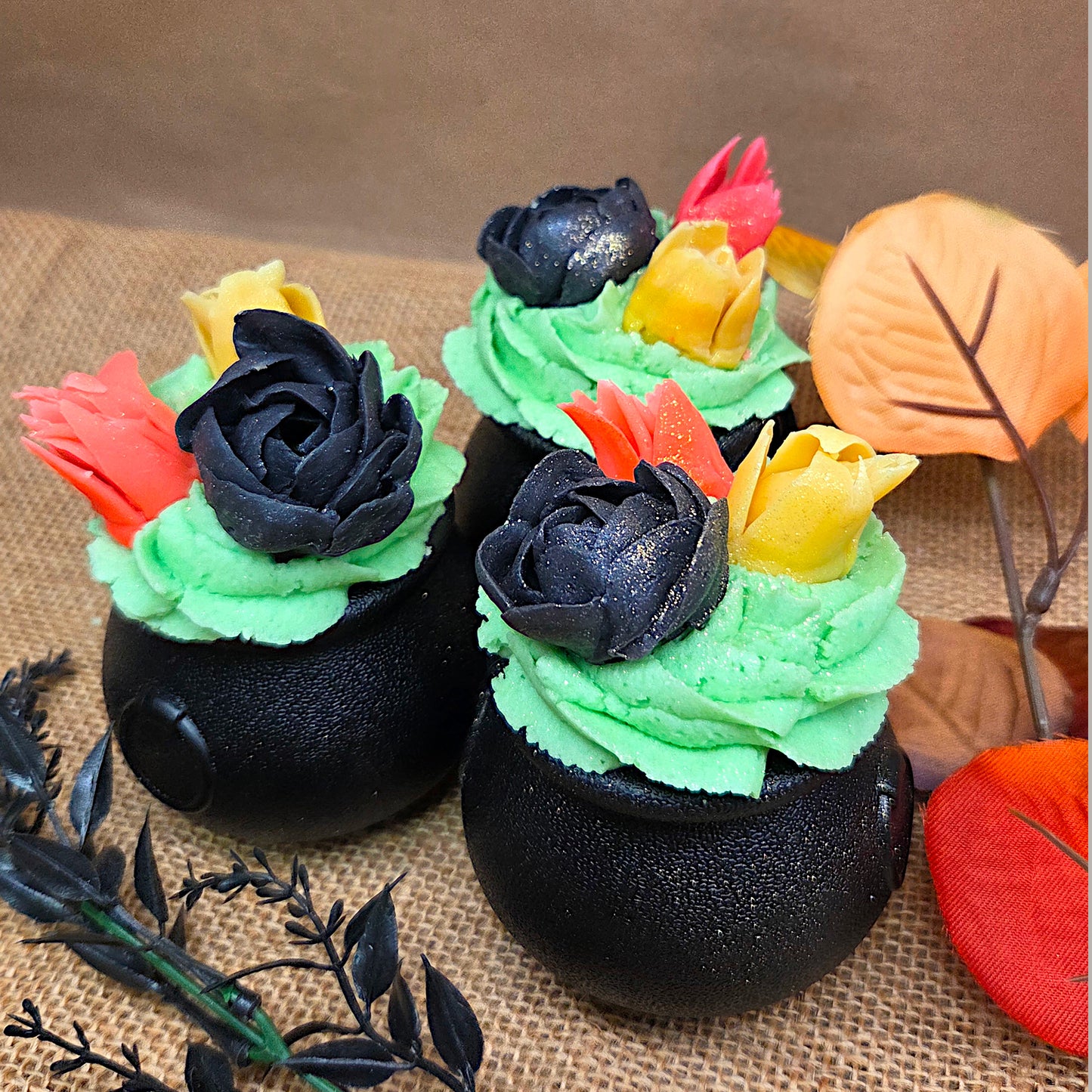 three black cauldrons with green, black, red, and yellow flowers on top