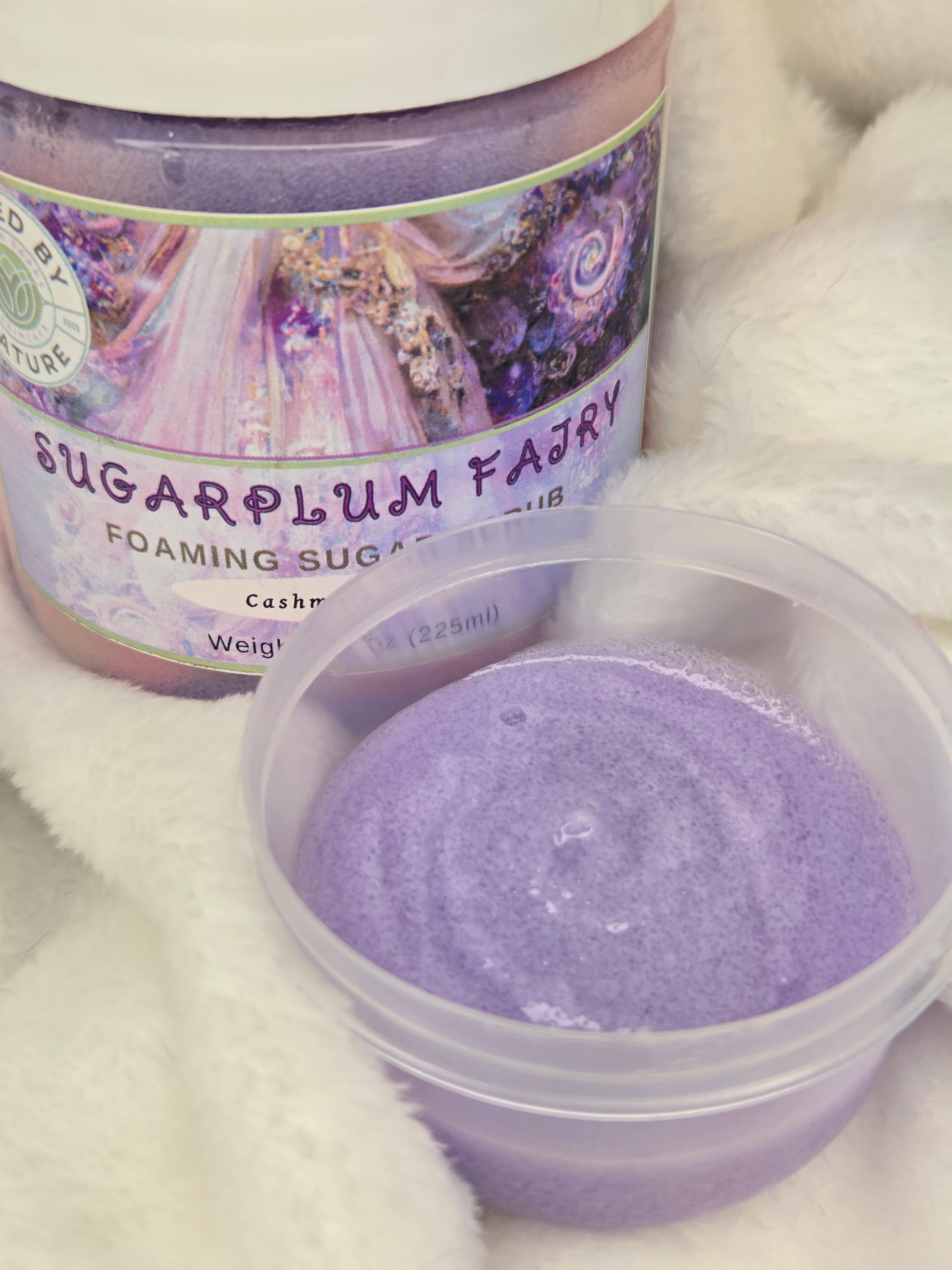Purple foaming sugar product with a label on a white fluffy background, with a sample next to it for content texture.