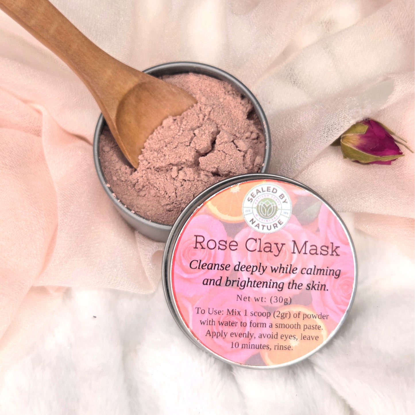 Rose Clay Mask in a tin with a wooden spoon on a soft pink background