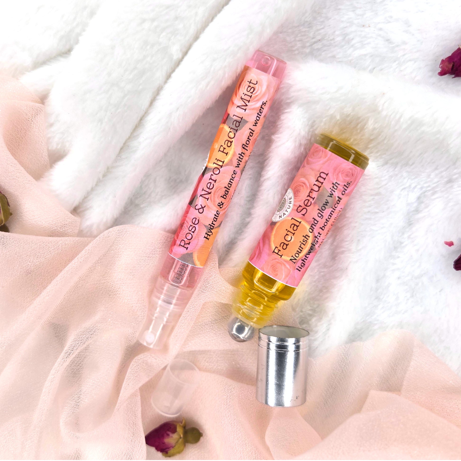 Two skincare products, a facial mist and serum, on a soft fabric background with rose petals.