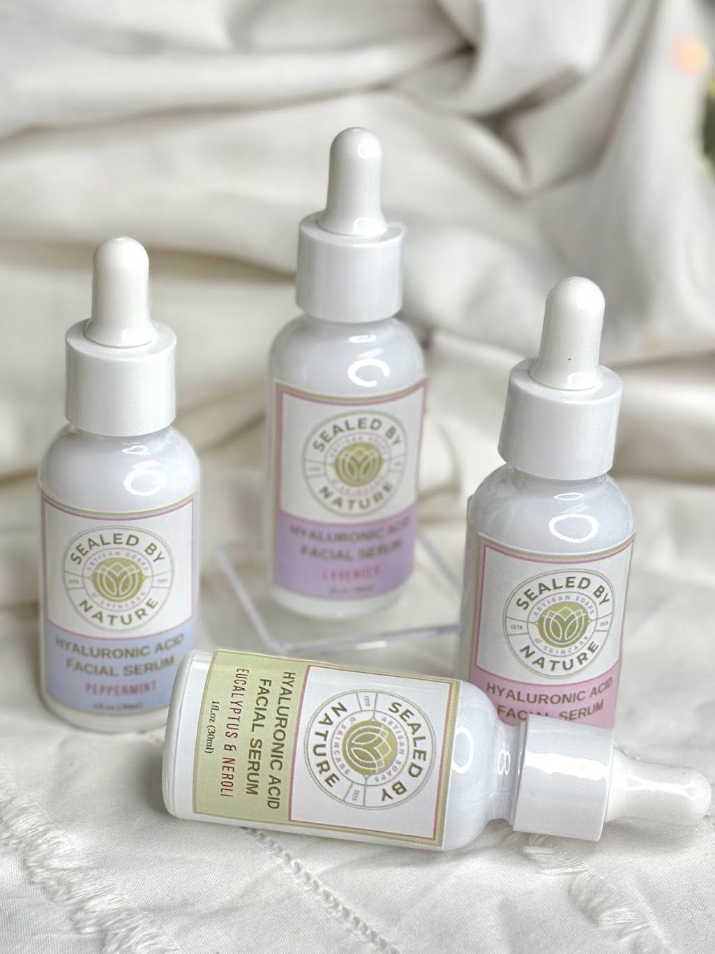 Four skincare serum bottles labeled 'Sealed by Nature' on a textured white surface.
