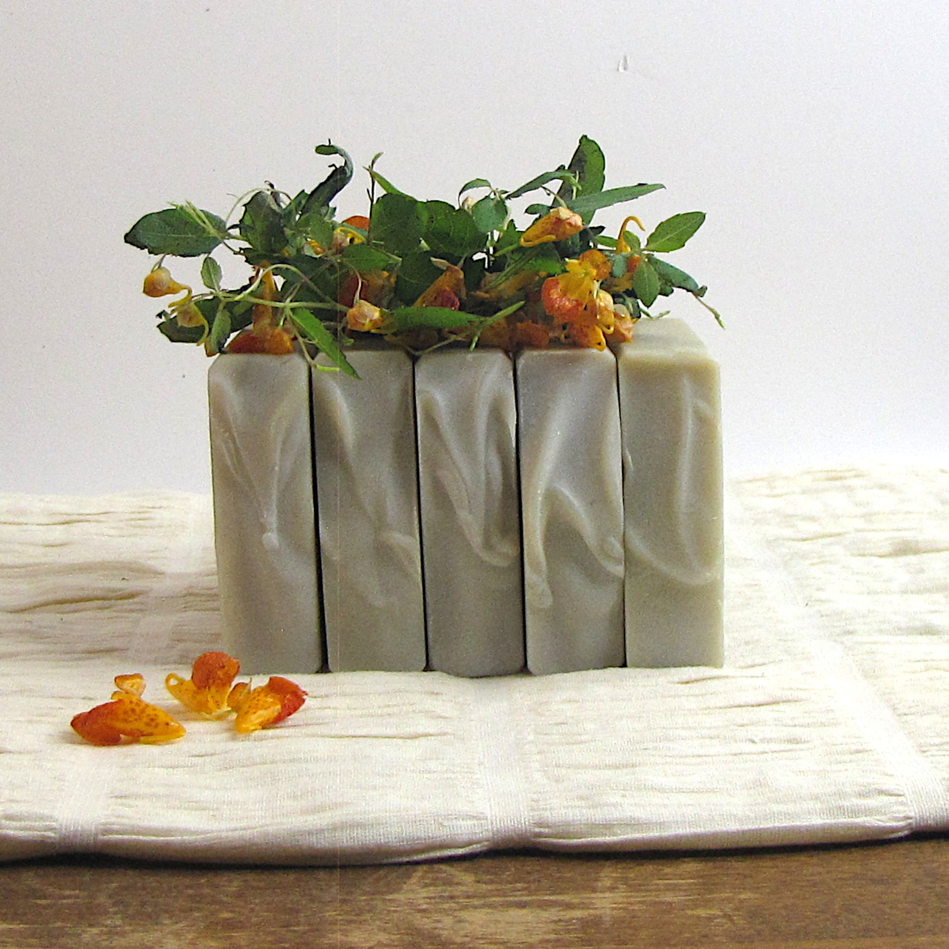 Four bars of soap with greenery and flowers on a white surface
