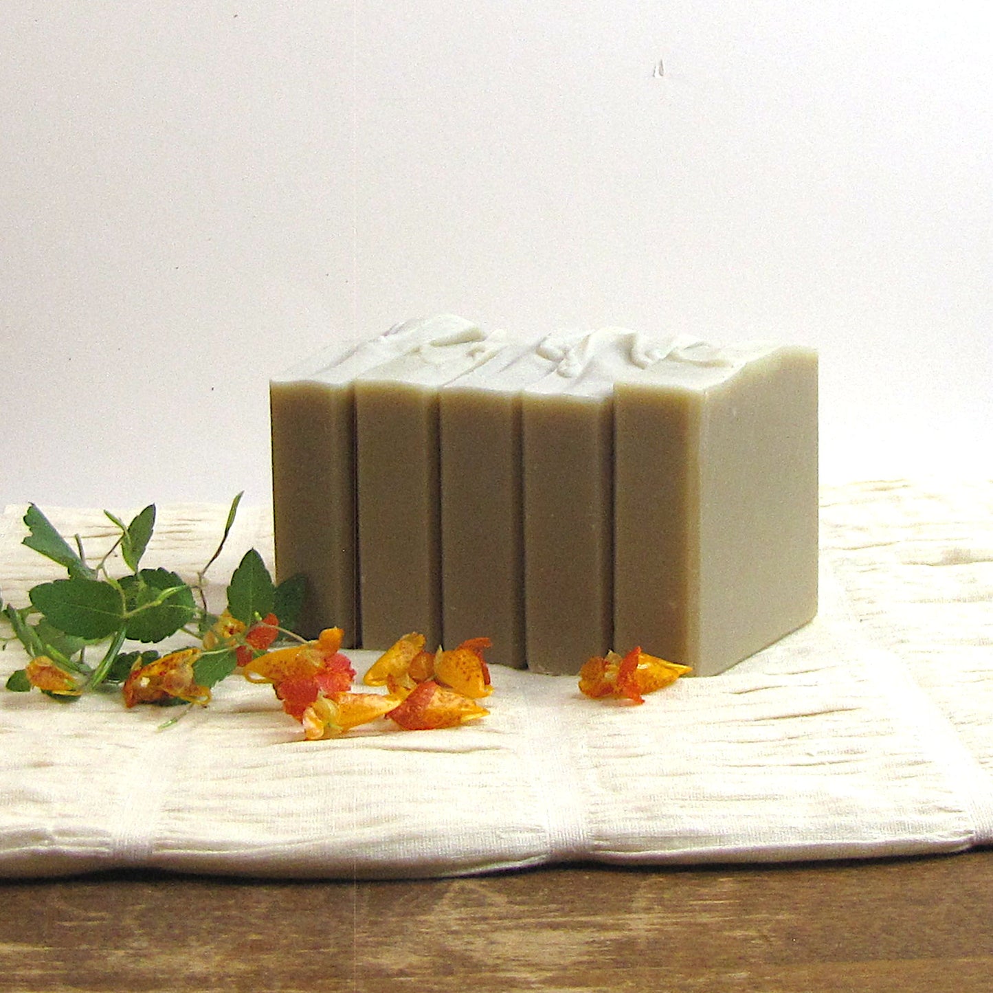 Five bars of soap on a white surface with greenery and flowers.