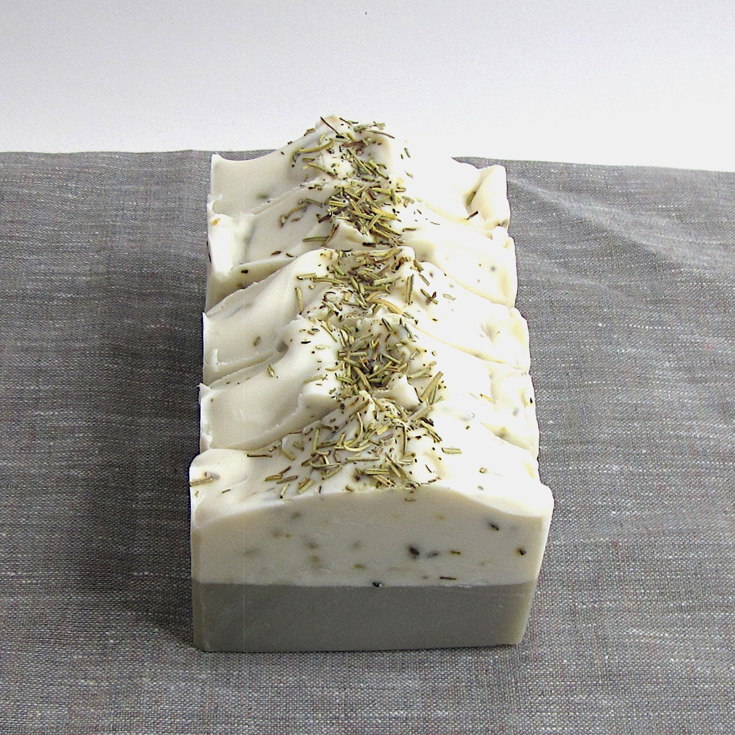 Bars of soap with dried Rosemary leaves on a gray fabric background