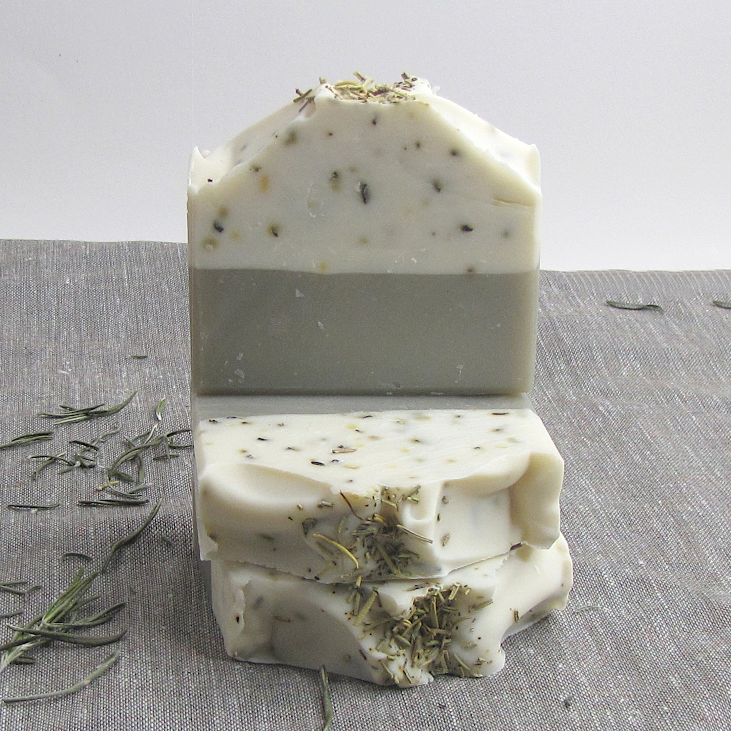 Stack of layered soap bars with herbs on a textured surface