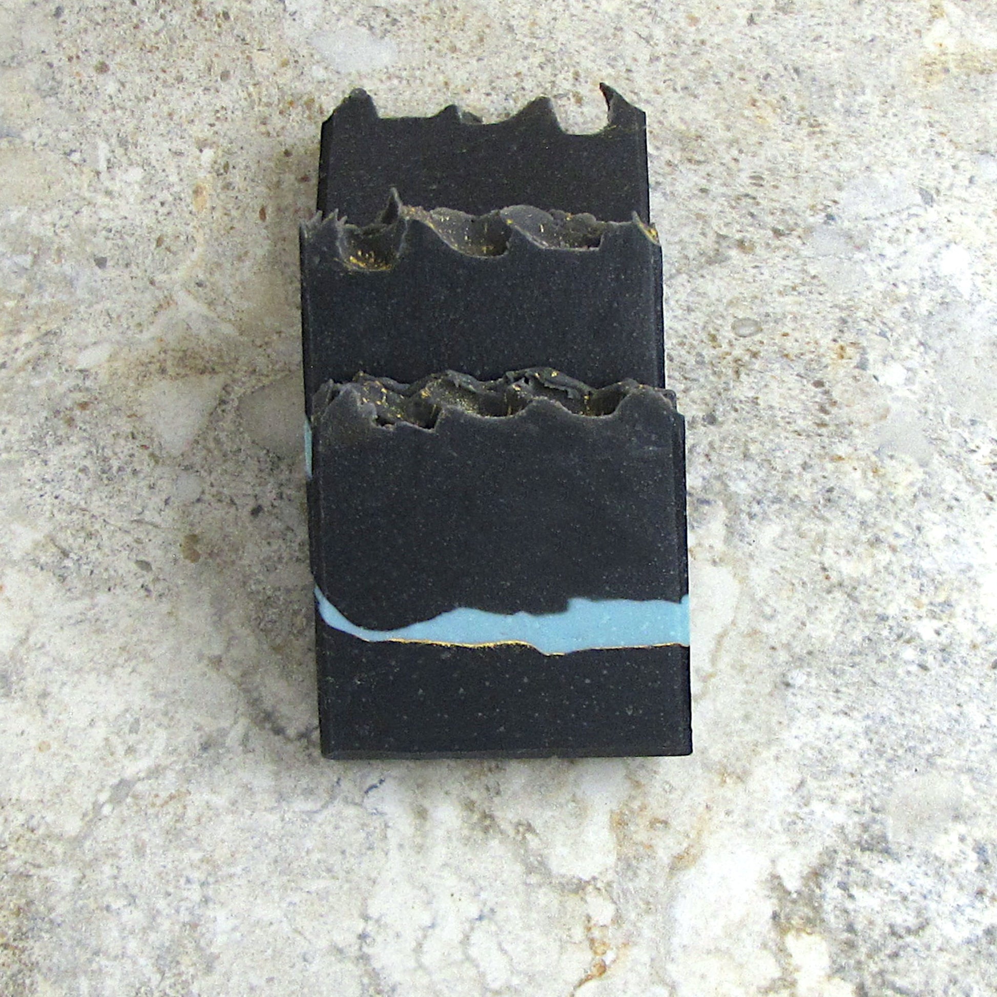 Charcoal soap bar with Pumice powder. A thin layer of blue across the center and a gold mica line.   