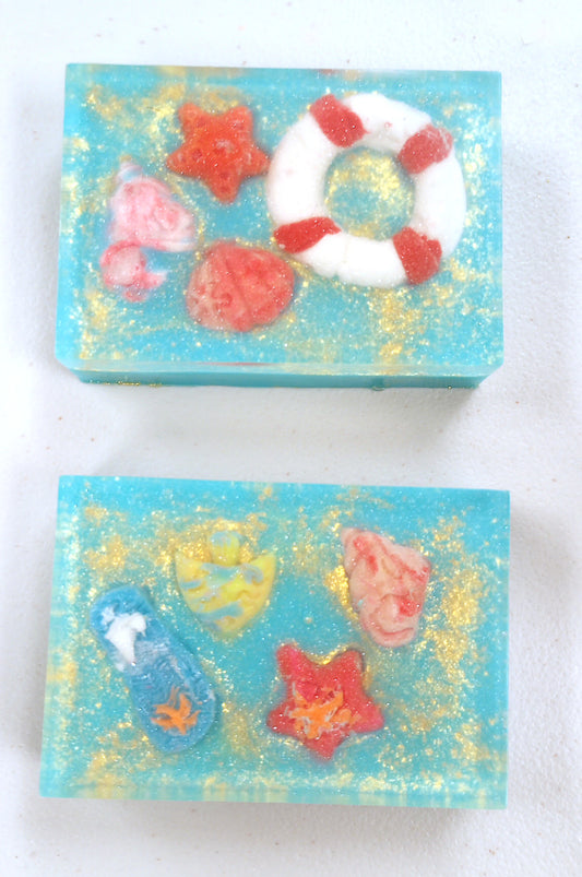 Two decorative soap bars with starfish, shells, and a life buoy on a white background