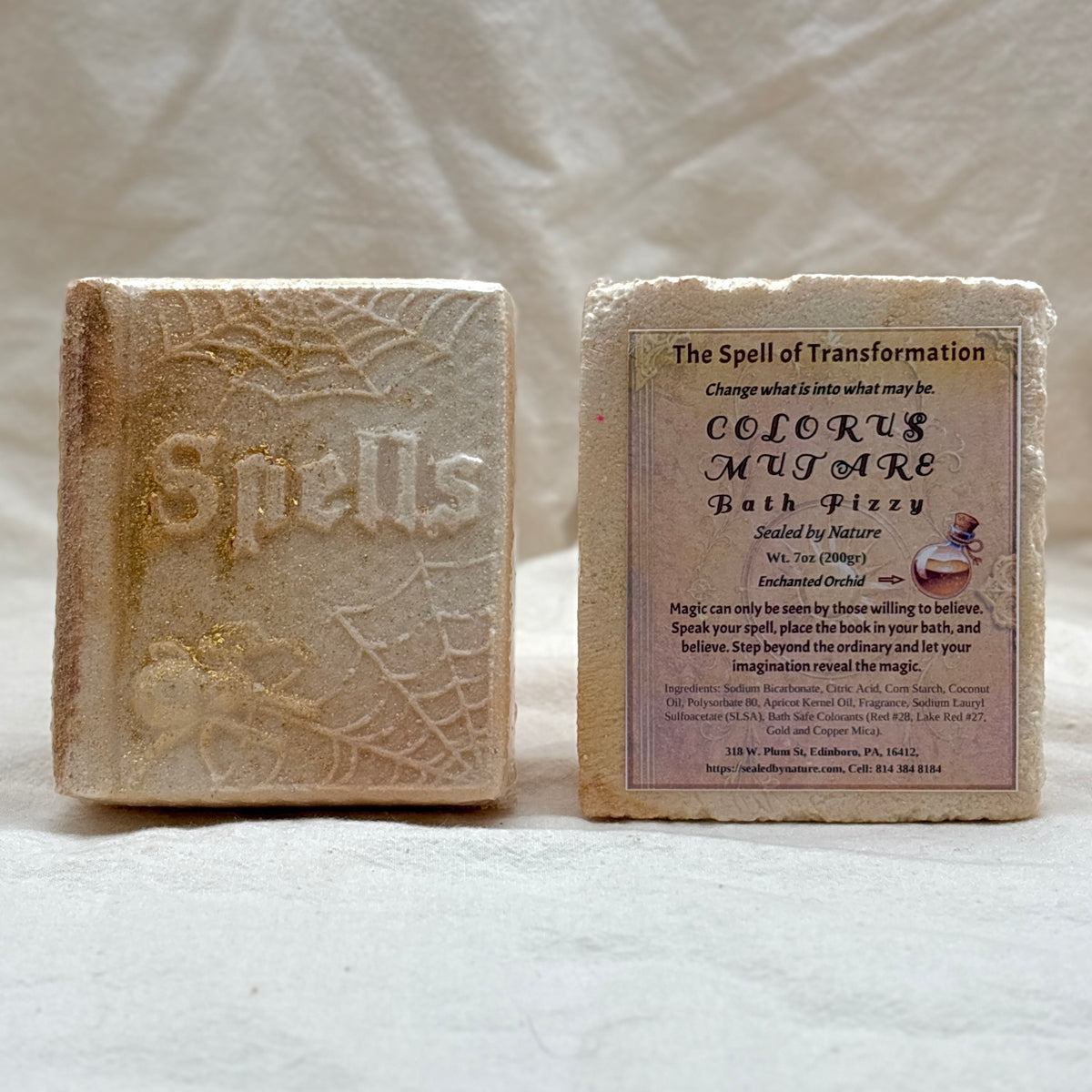 Two rectangular bath bombs shown side by side on a light fabric background. The left bath bomb is textured and embossed with the word 'Spells.