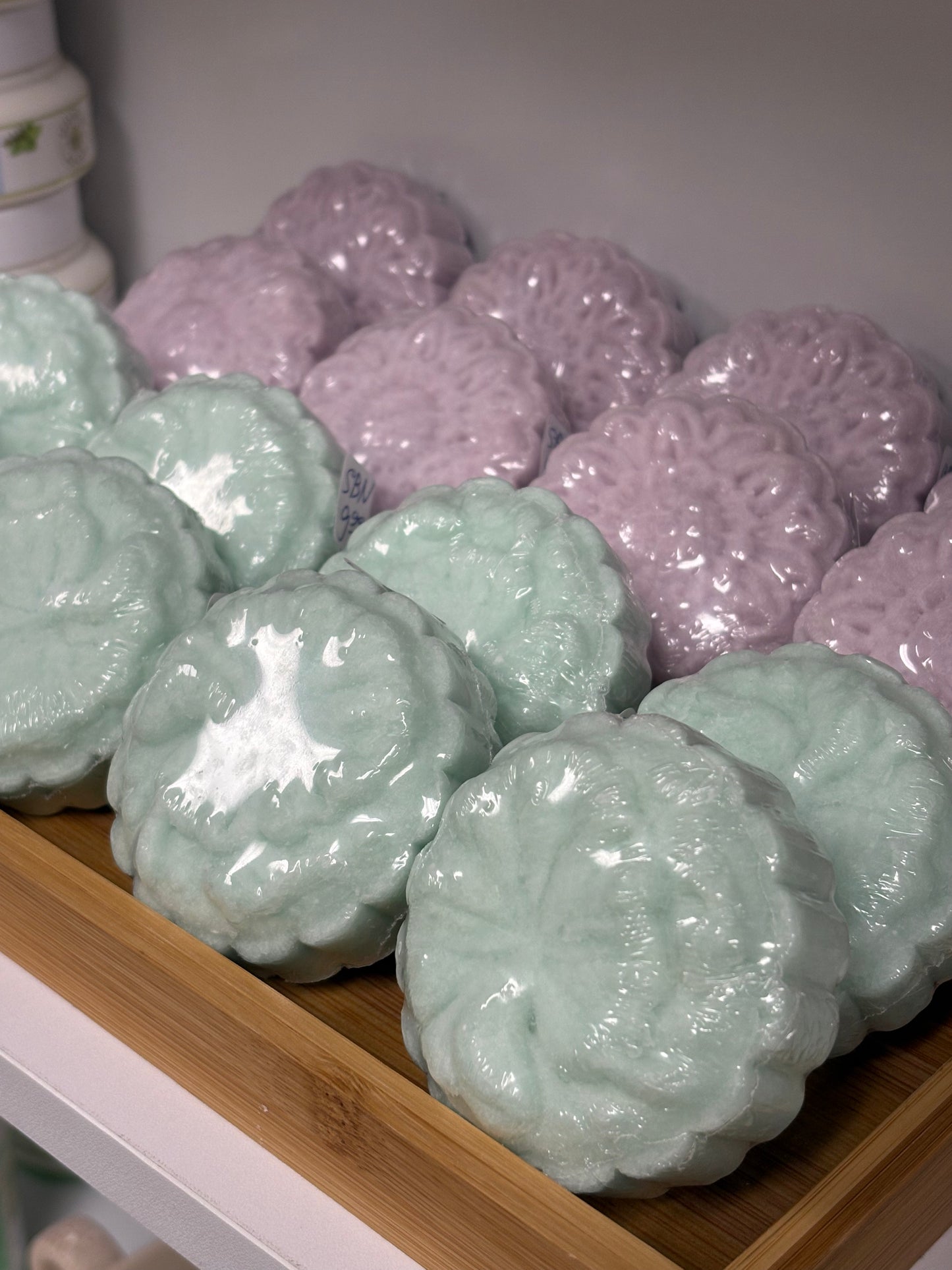 Shampoo bars in light teal and purple on a wooden shelf.