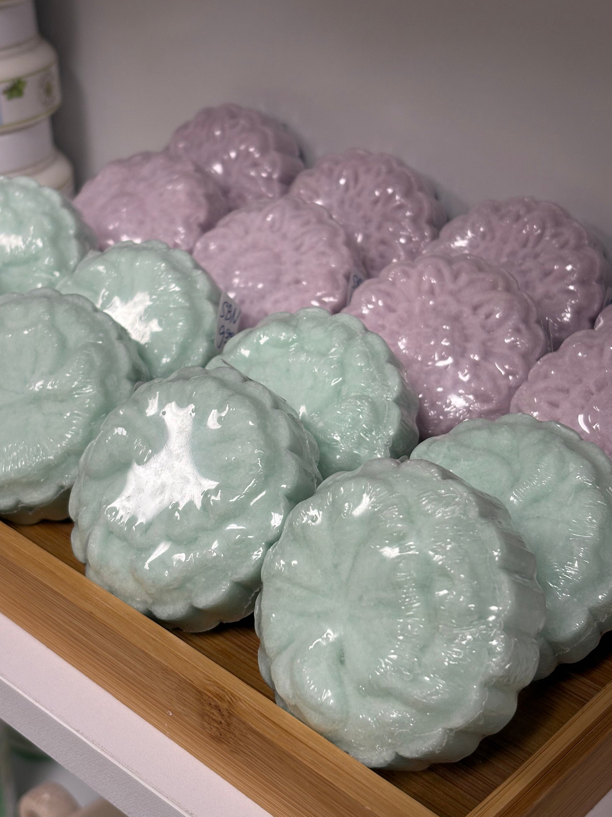 Shampoo bars in light teal and purple on a wooden shelf.