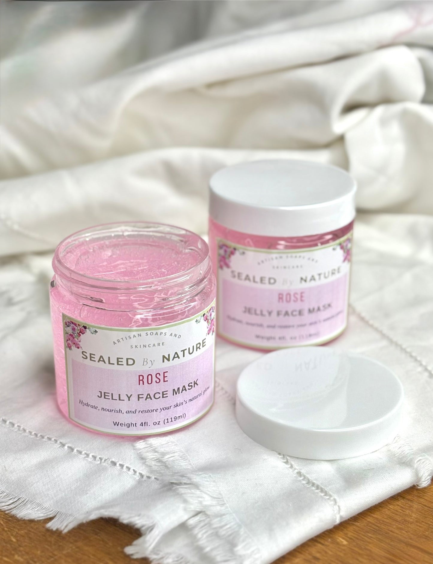 Two jars of Sealed by Nature Rose Jelly Face Mask on a white fabric background