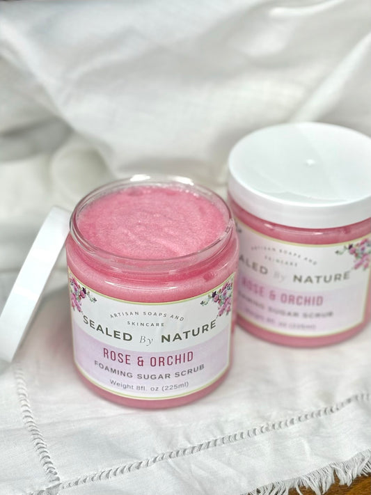 Two jars of Sealed by Nature Rose & Orchid foaming sugar scrub on a white fabric background.