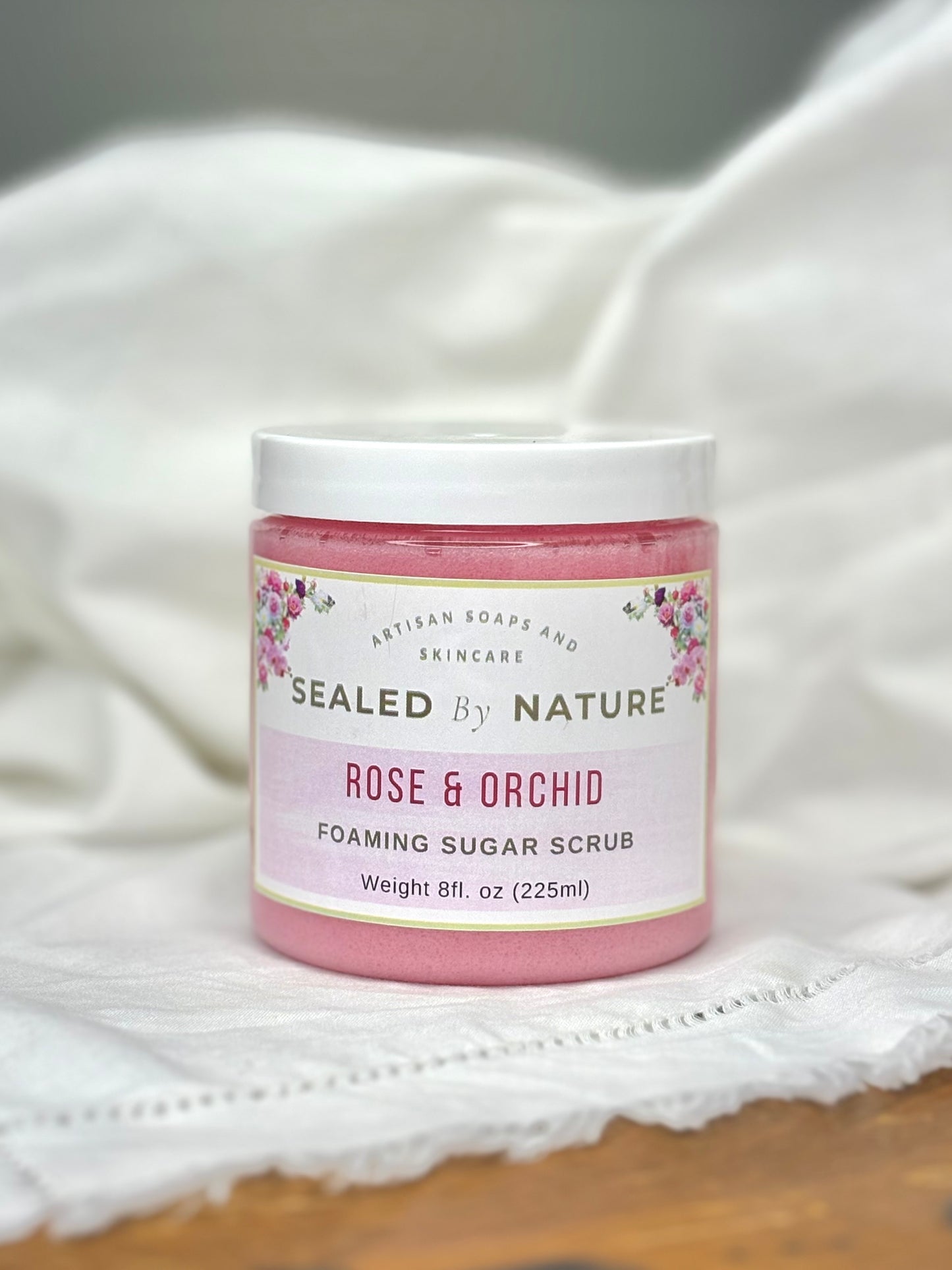 Pink jar of Sealed by Nature Rose & Orchid Foaming Sugar Scrub on a white fabric background