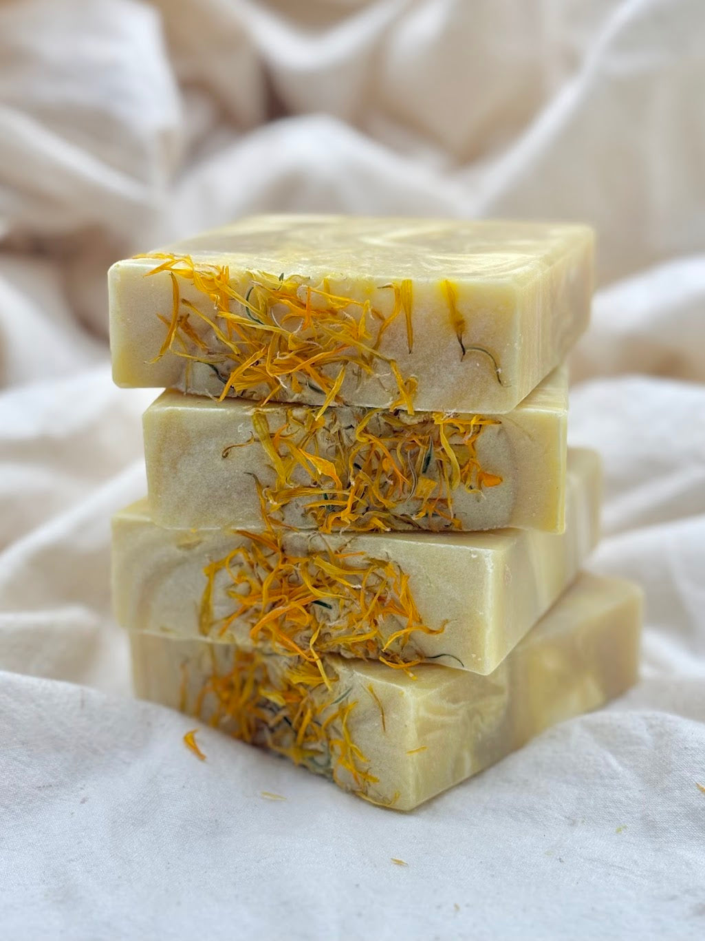 Stack of three rectangular soap bars with visible yellow flecks on a white fabric background