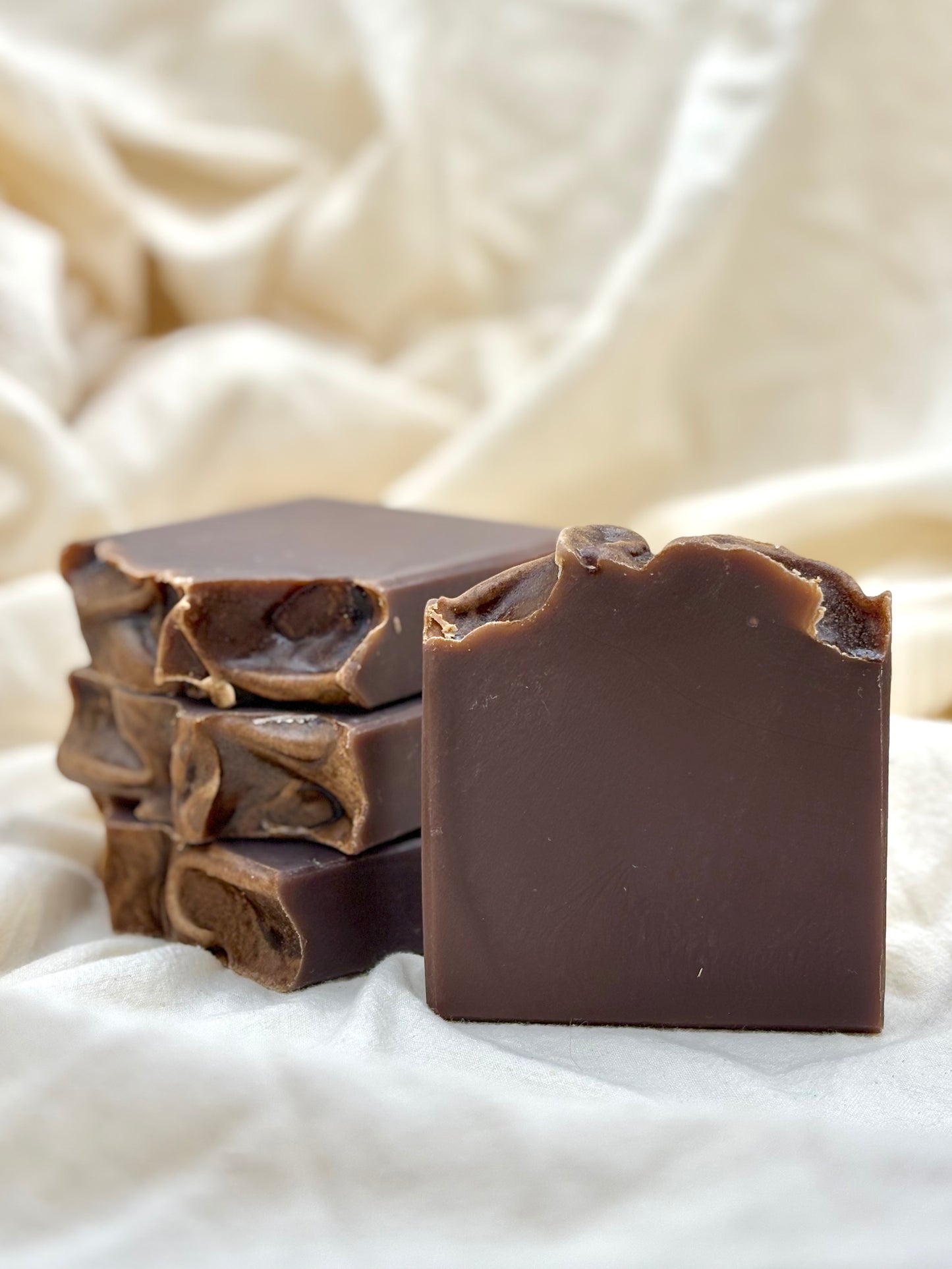Stack of dark chocolate soap bars on a textured white fabric background