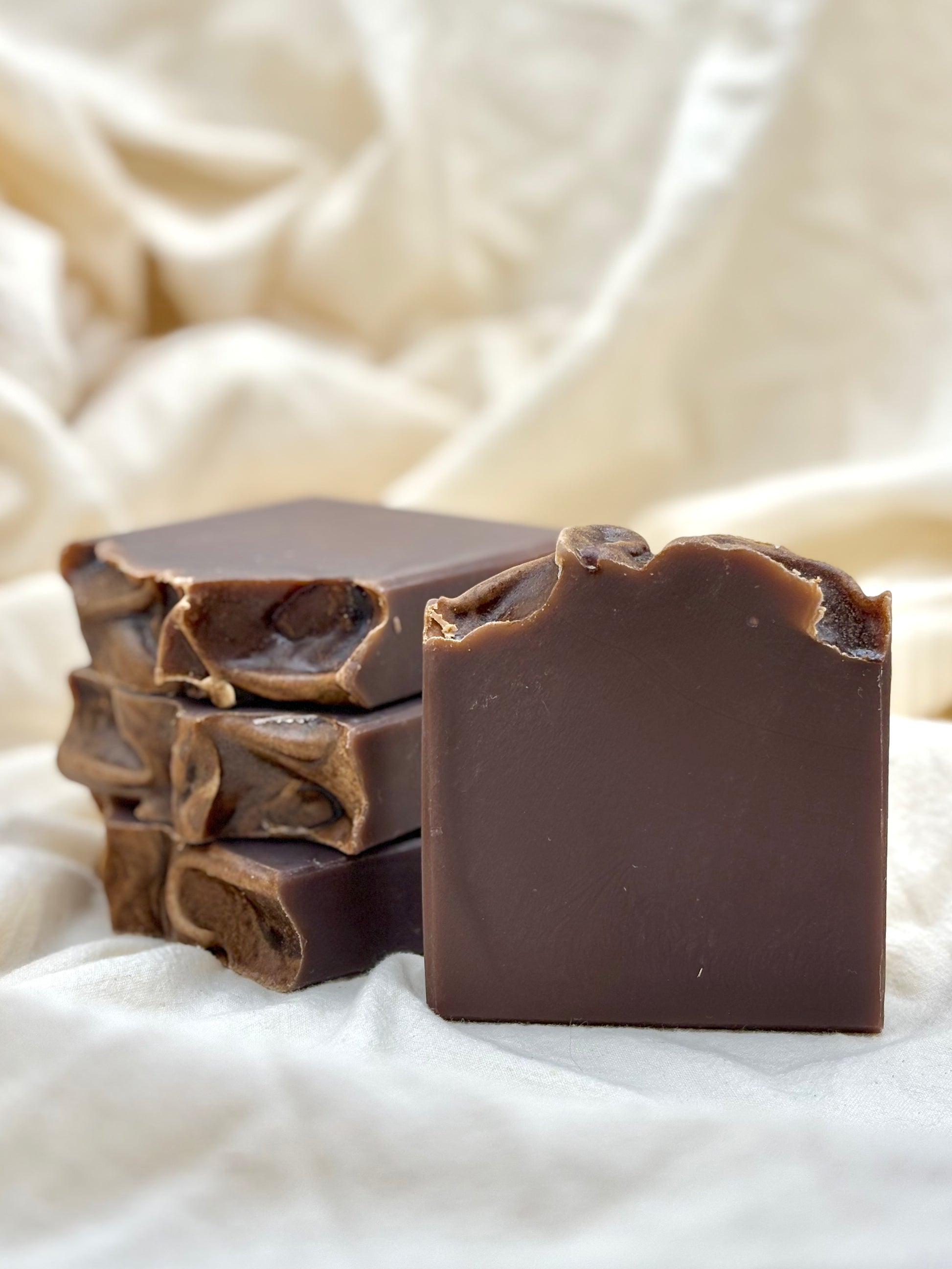 Stack of dark chocolate soap bars on a textured white fabric background