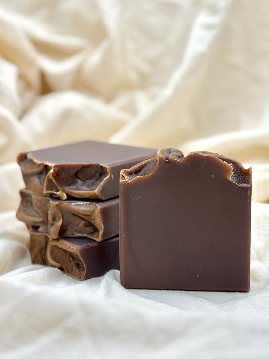 Stack of dark chocolate soap bars on a textured white fabric background