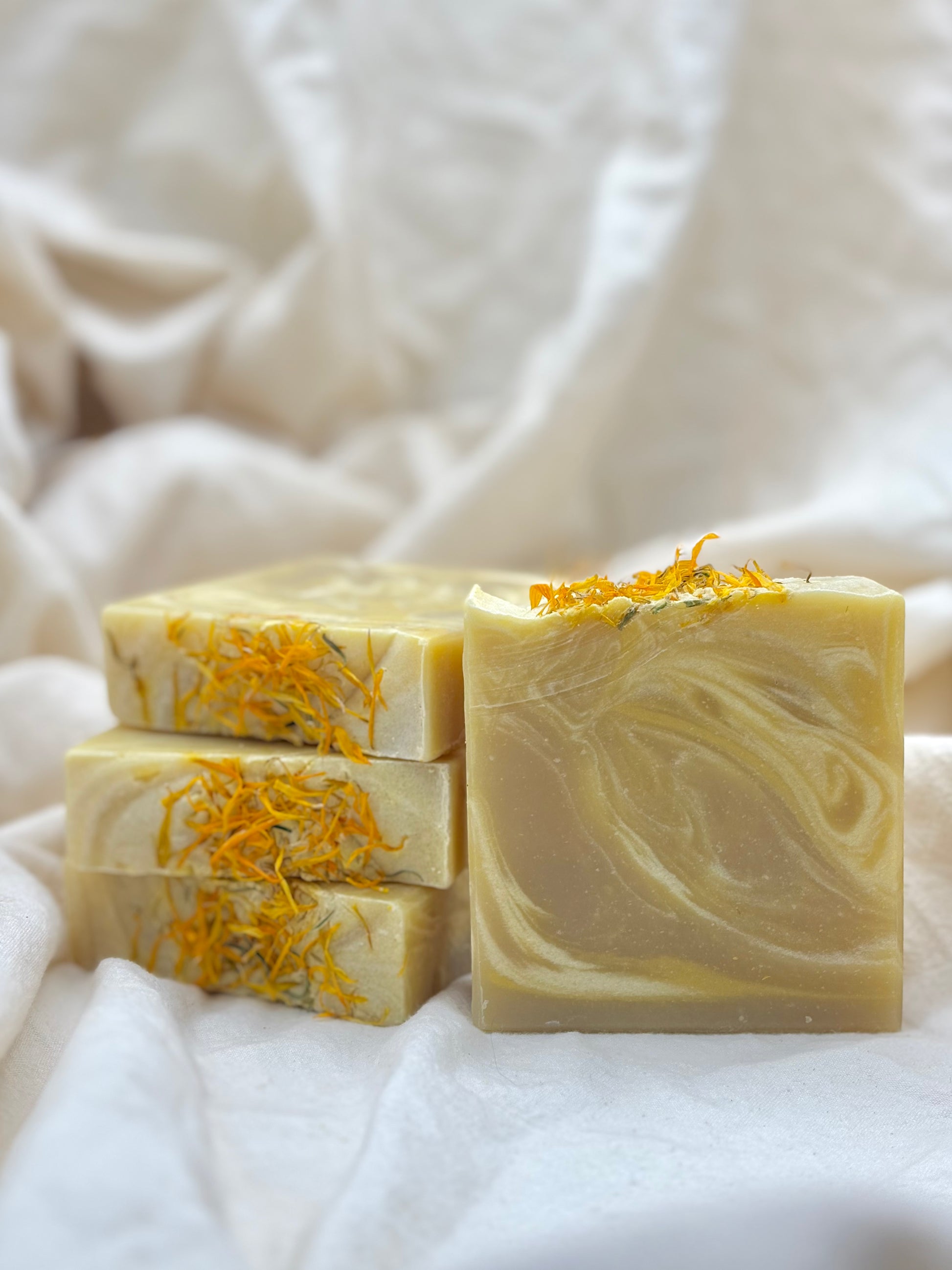 Three bars of soap with orange zest on a white fabric background