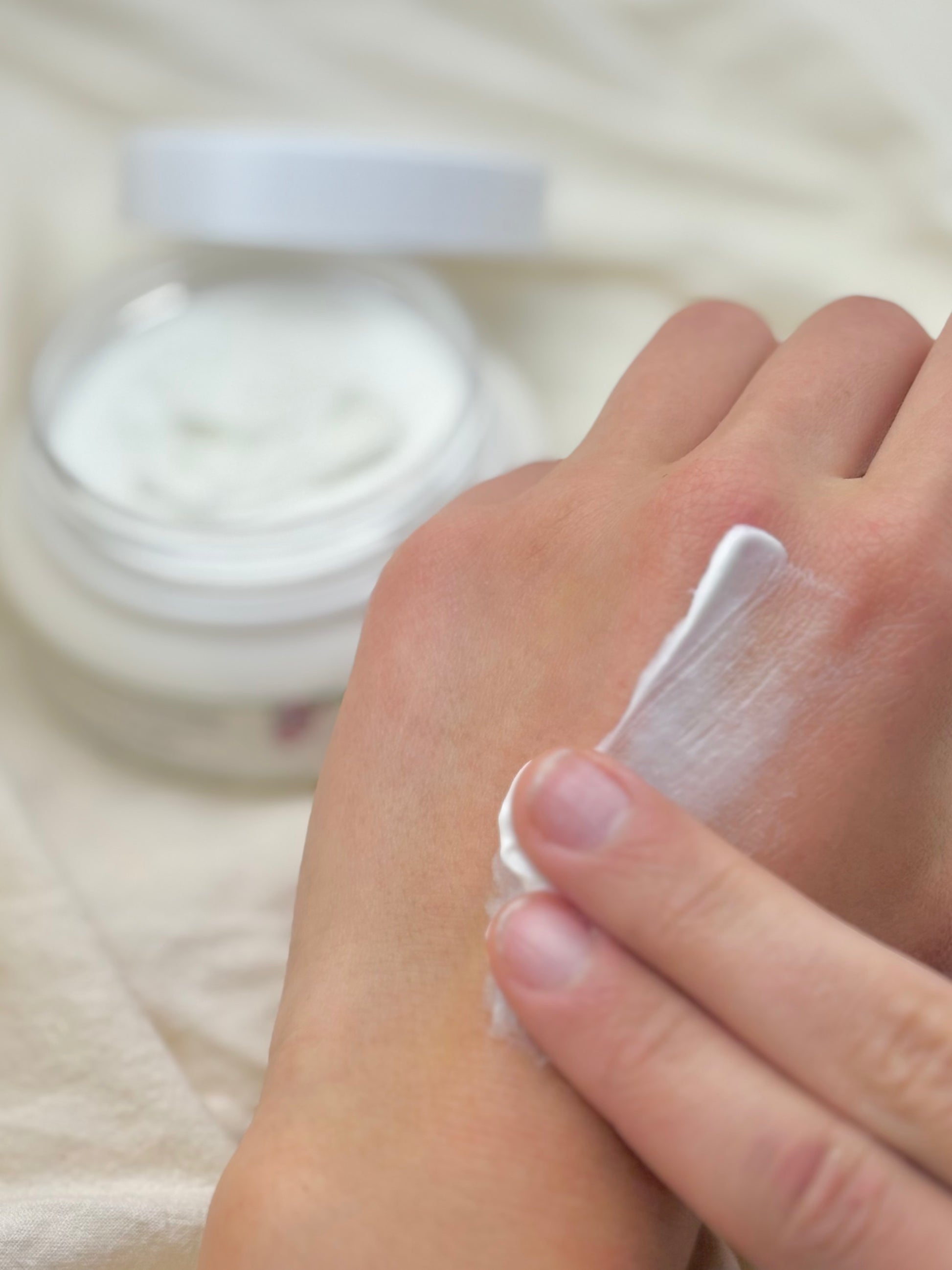 Hand applying cream to hand with a jar of cream in the background