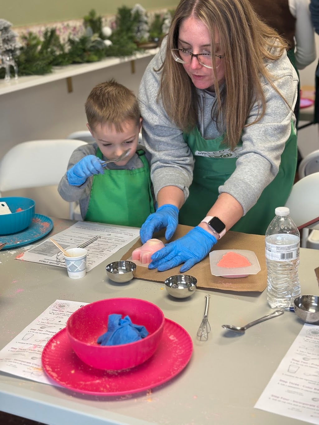 A woman and a child in green aprons molding bath bombs.