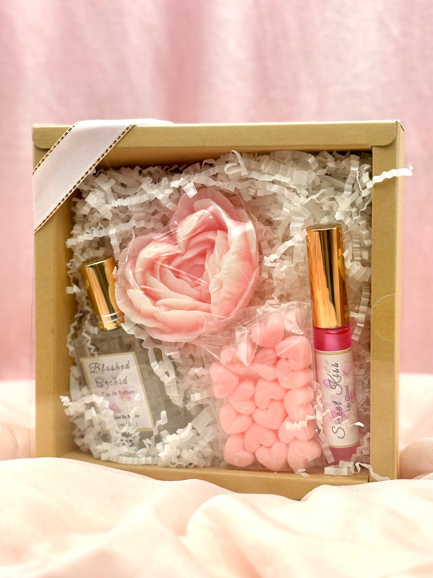 Gift set with Perfume, lip gloss, and soap flower, solid lotion on a pink background.