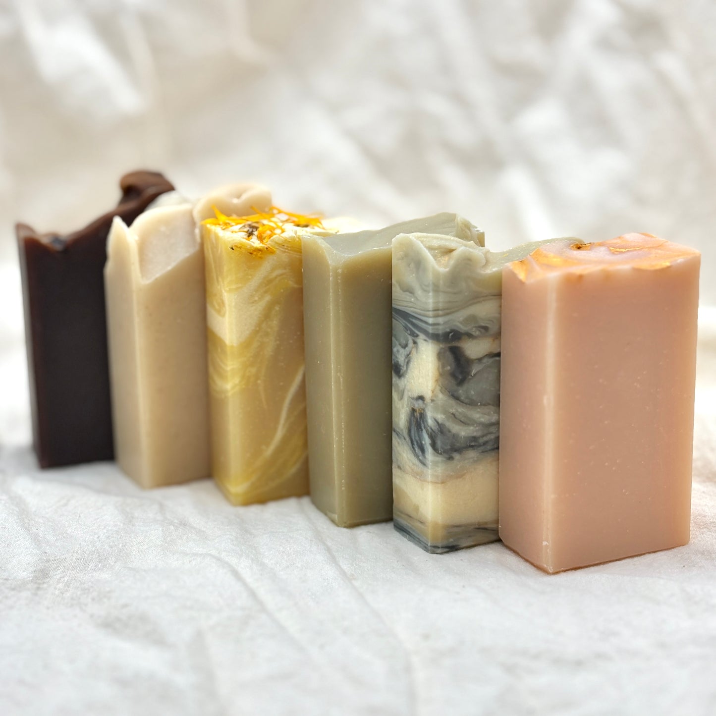 Five bars of soap with different colors and textures on a white fabric background
