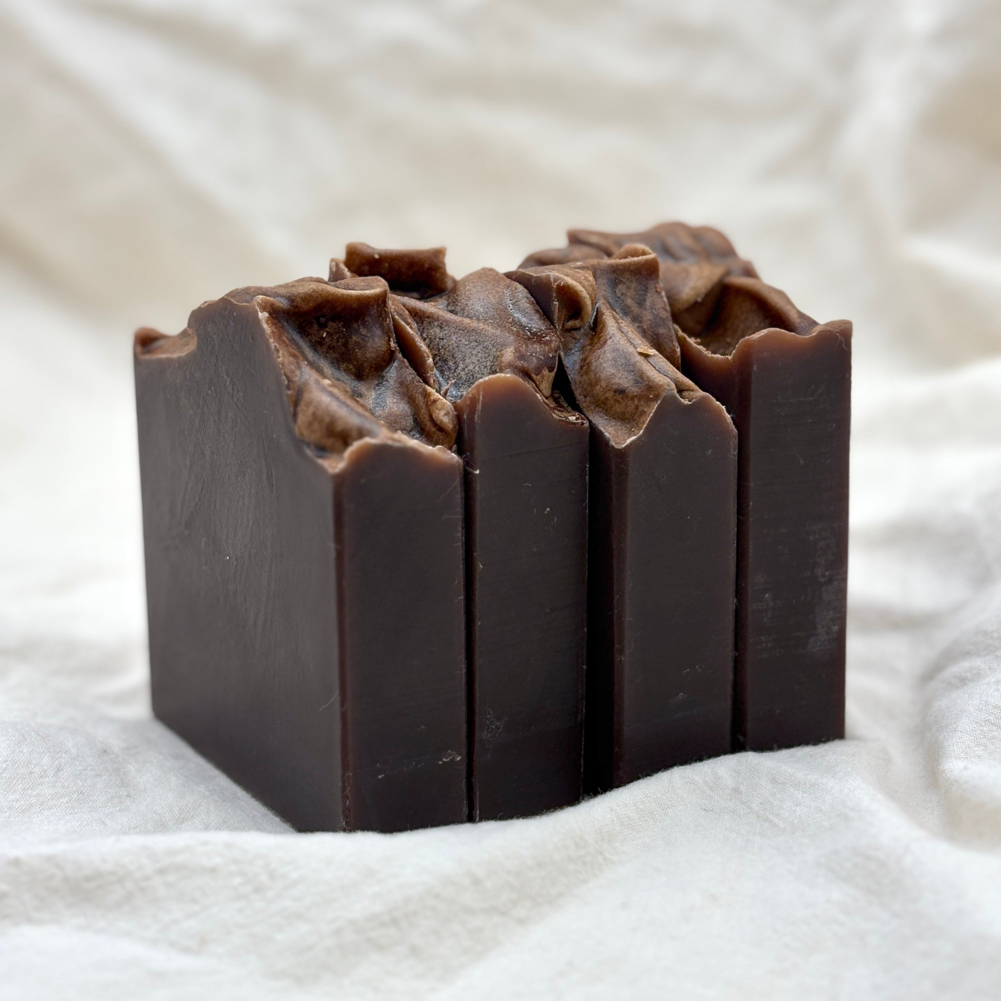 Dark brown soap bar with textured surface on a white fabric background
