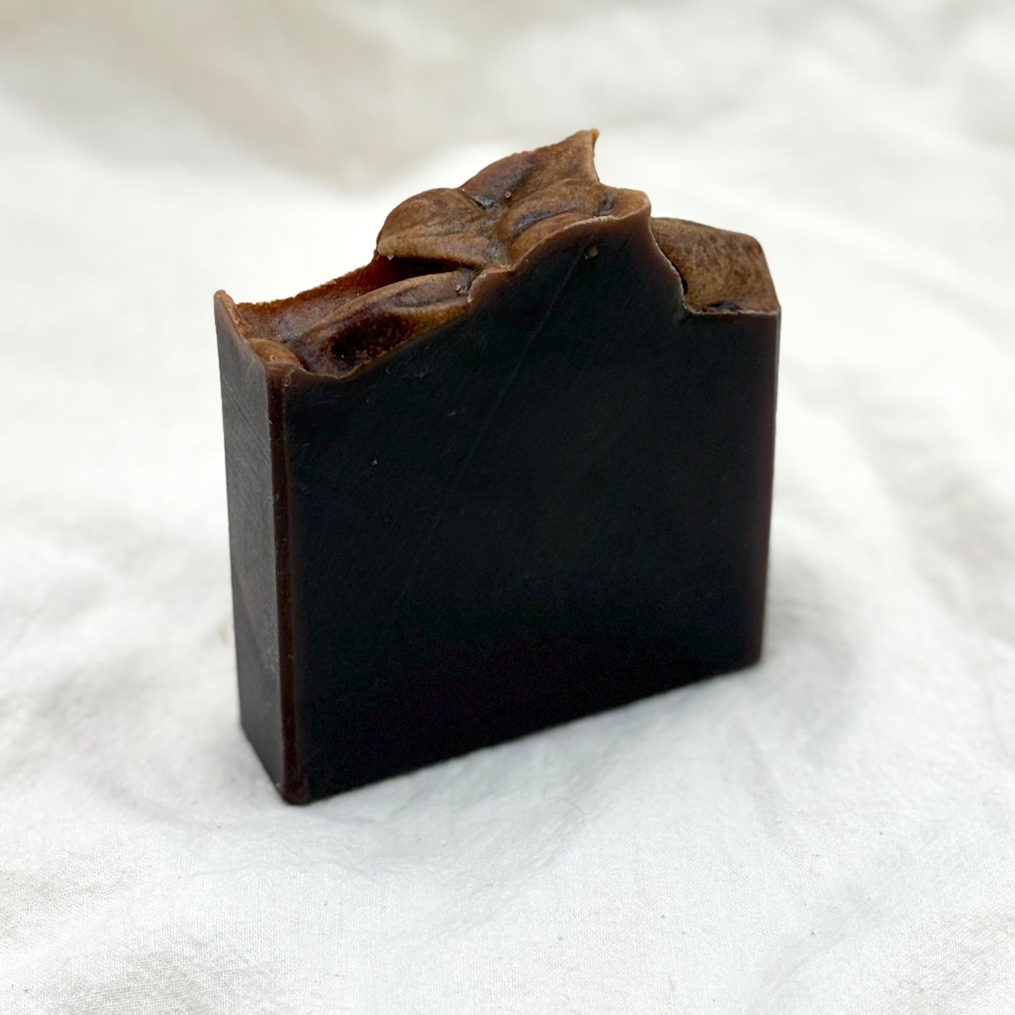 Dark brown soap bar with leafy top on a white background
