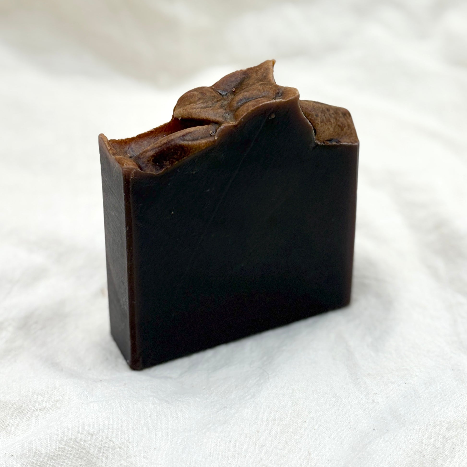 Dark brown soap bar with leafy top on a white background