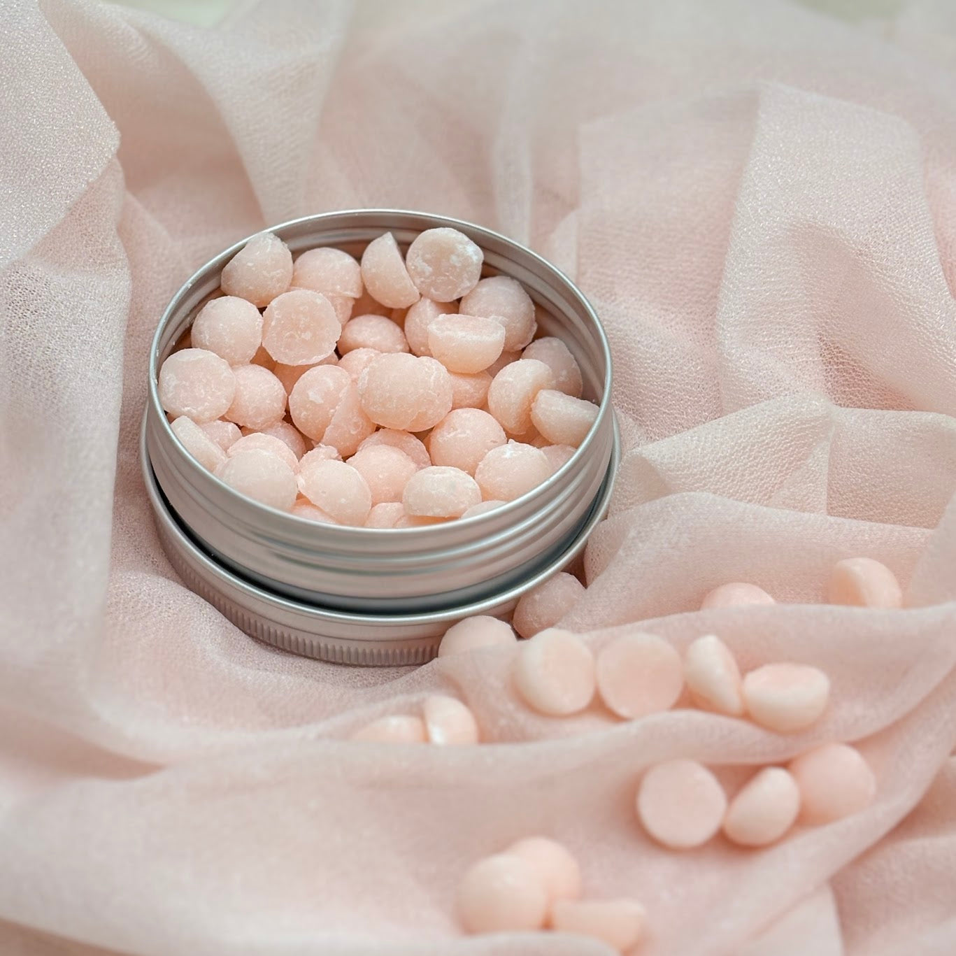 Silver tin filled with pink heart-shaped candies on a soft pink fabric background