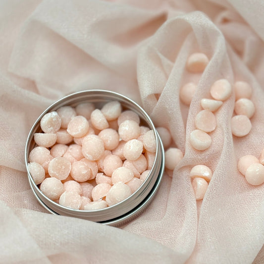 Small metal container filled with round, pinkish-white objects on a soft, light fabric background.
