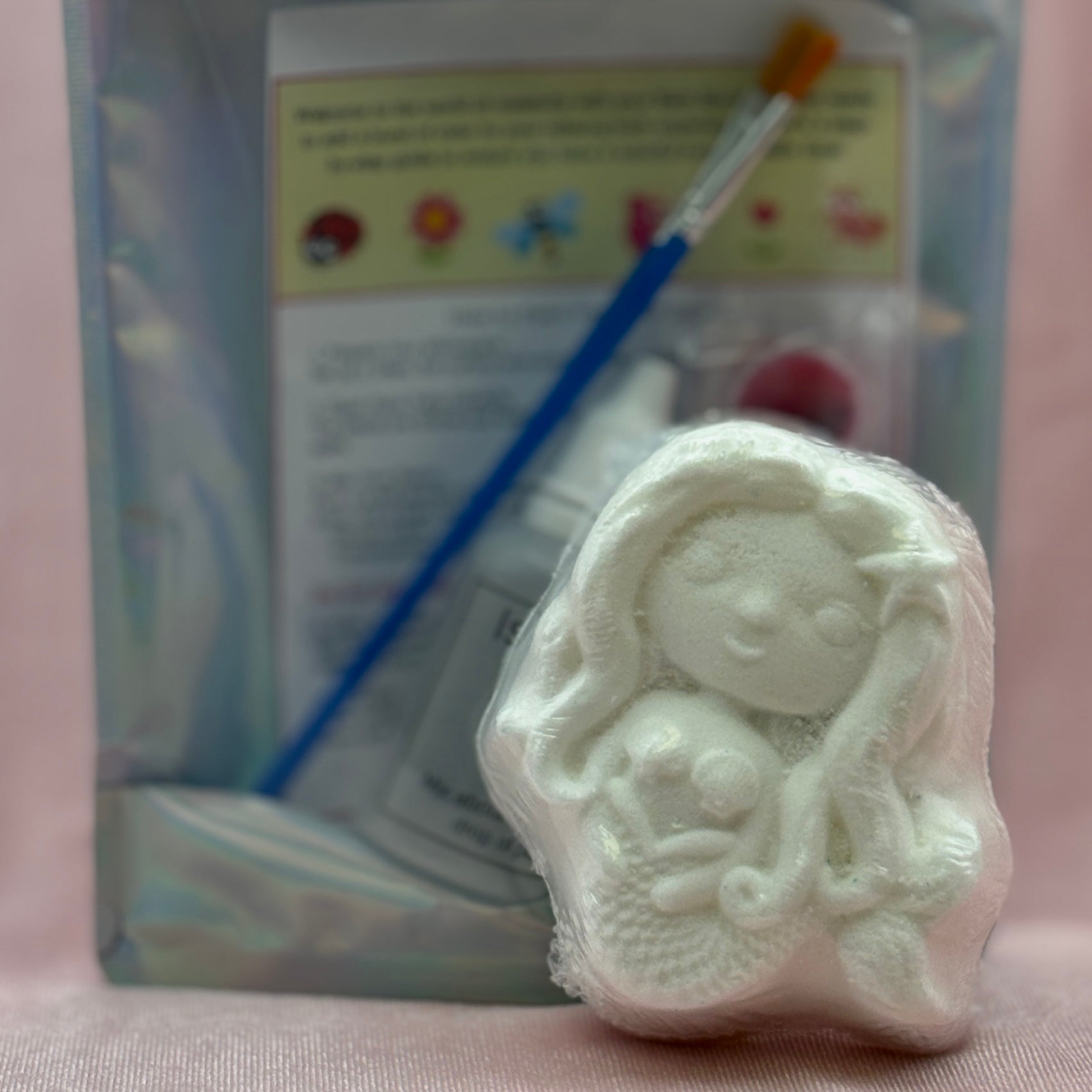 White mermaid bath bomb for painting with paintbrush and paint palette in the background