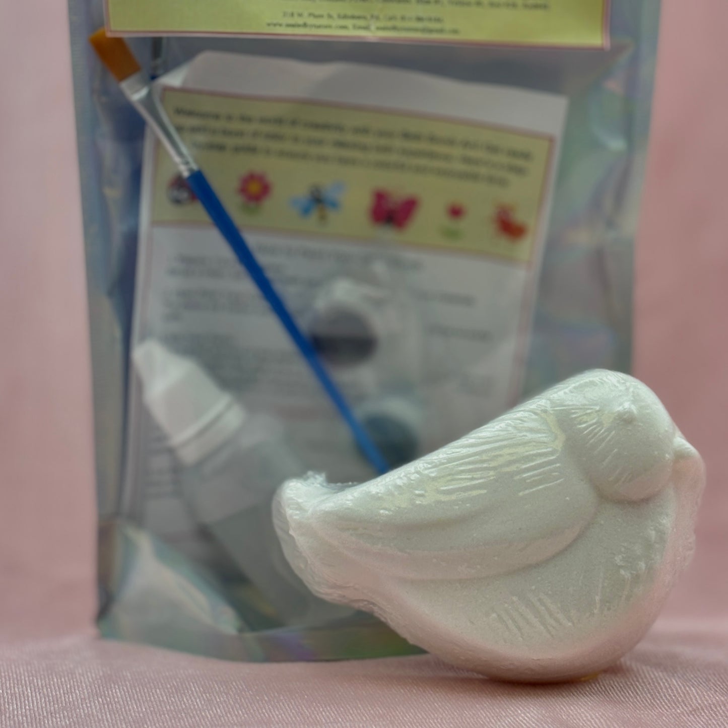 White bath bomb bird with paintbrush and packaging in the background