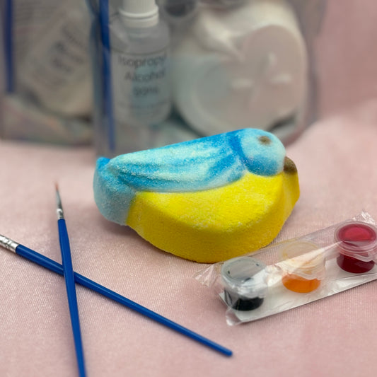 Colorfully painted bird-shaped bath bomb with painting supplies on a pink surface