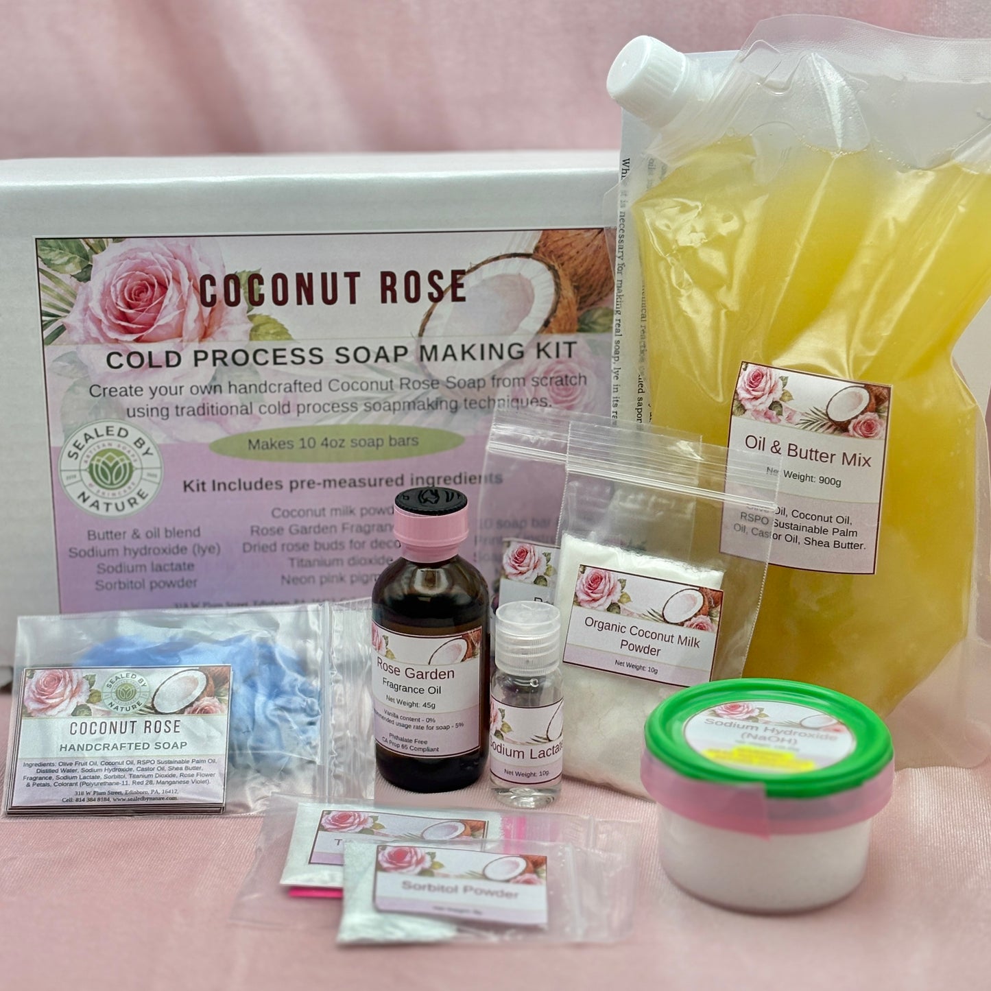Cold process soap making kit with various ingredients and packaging on a pink background