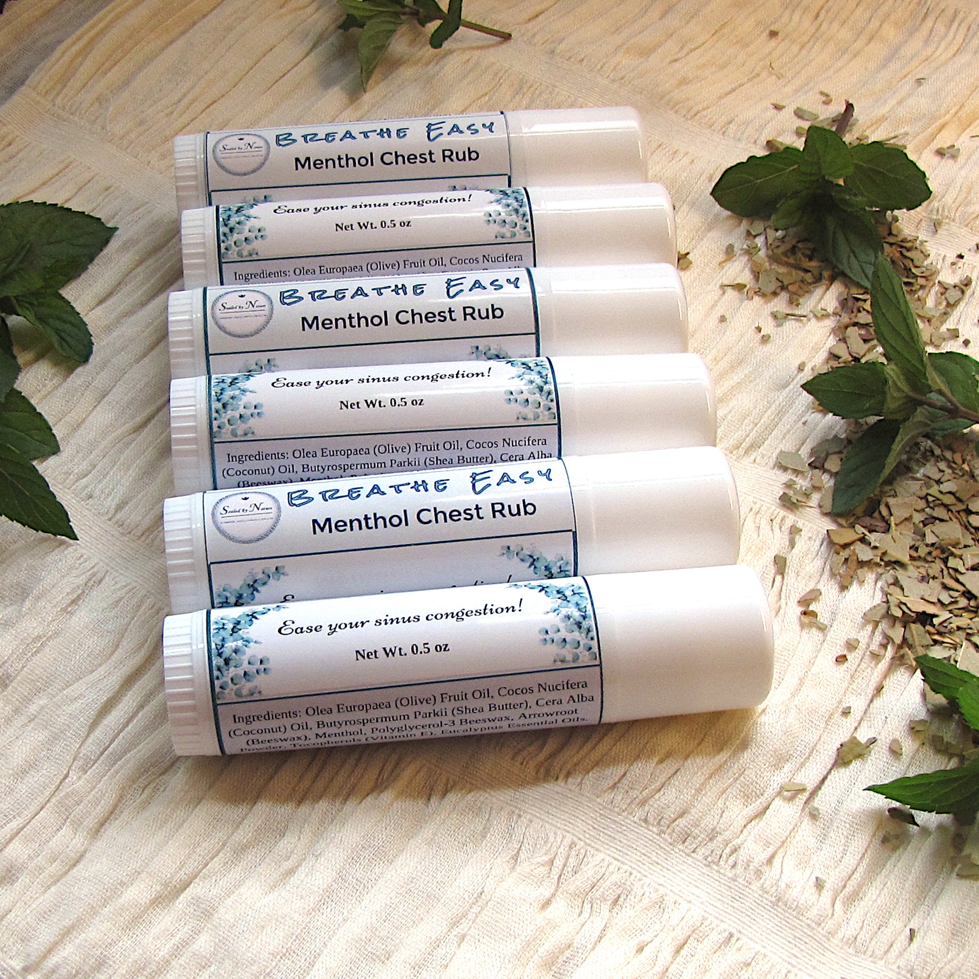 Stack of 'Breathe Easy' Menthol Chest Rub bottles on a wooden surface with herbs.
